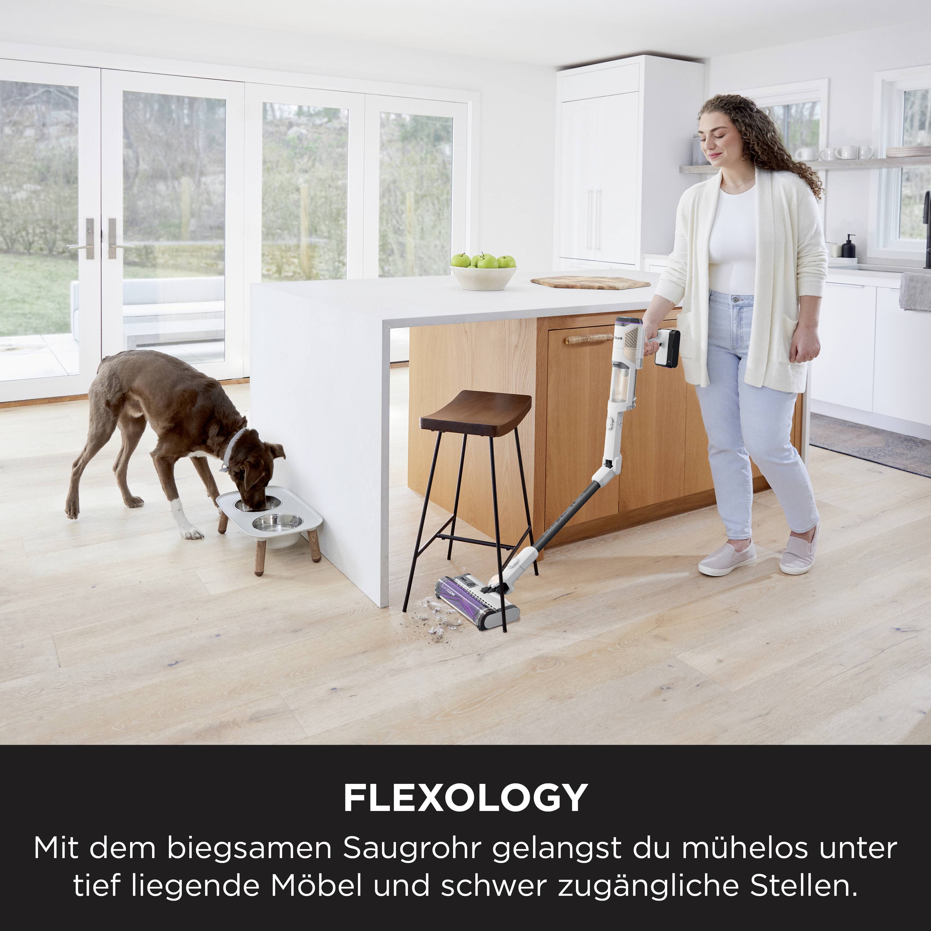 'Flexology: Mit dem liegenden Saugrohr erreichst du mühelos Stellen unter tief liegenden Möbeln.' Eine Frau saugt neben ihrem Hund.