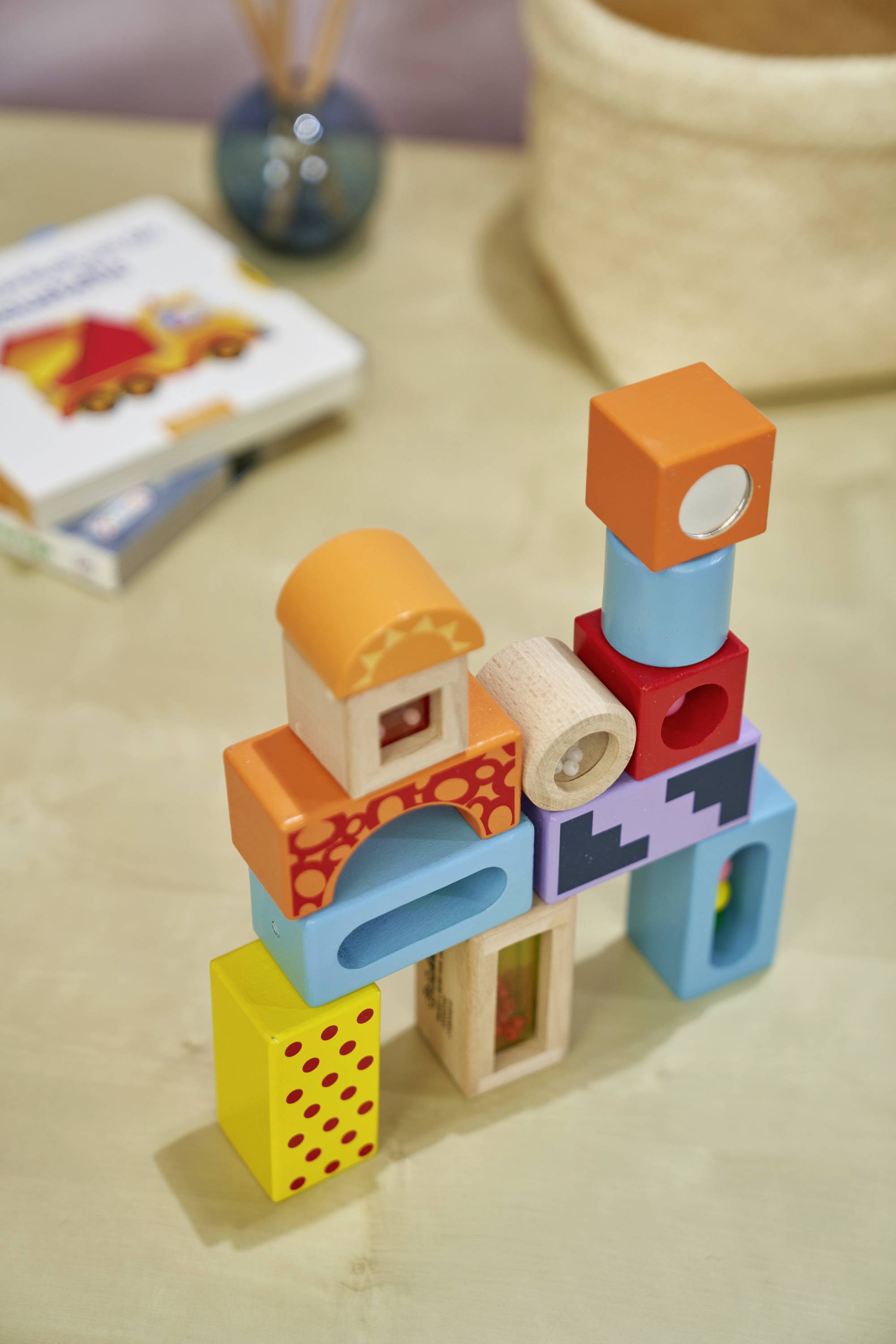 Ein bunter Turm aus Holzbausteinen steht auf einem Tisch. Im Hintergrund befindet sich ein Kinderbuch.