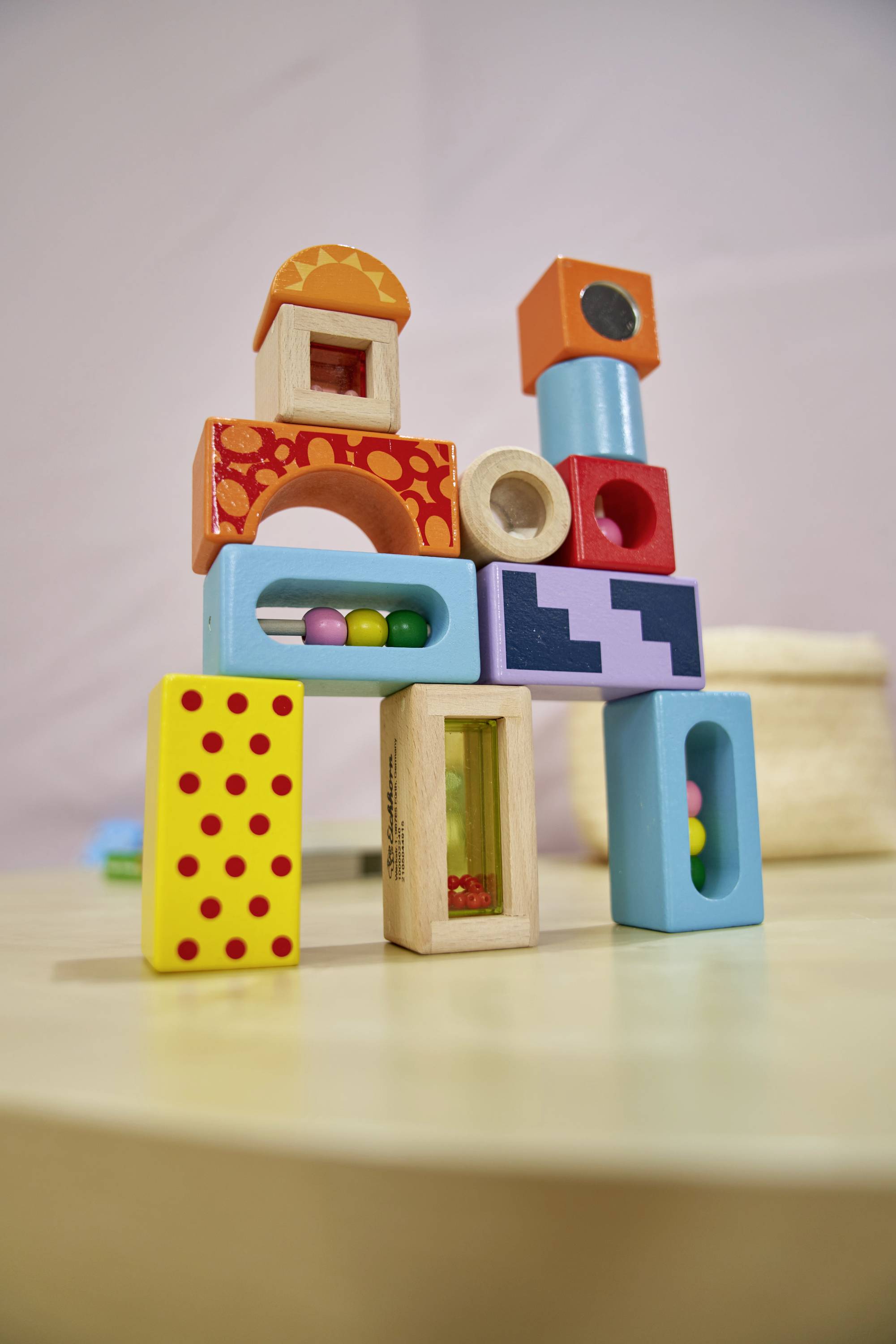 Bunte Holzbausteine auf einem Tisch gestapelt, verschiedene Formen und Muster, symbolisieren Kreativität und spielerisches Lernen.