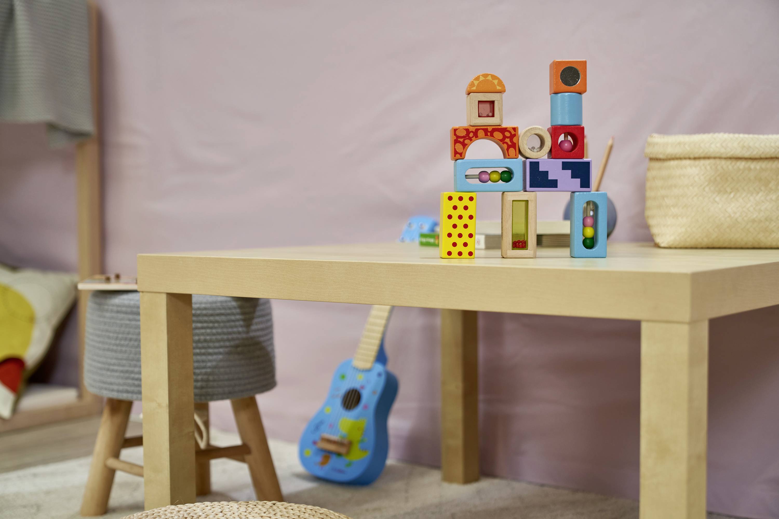 Holztisch im Kinderzimmer mit Bauklötzen darauf gestapelt. Im Hintergrund sieht man ein kleines blaues Spielzeuggitarre.