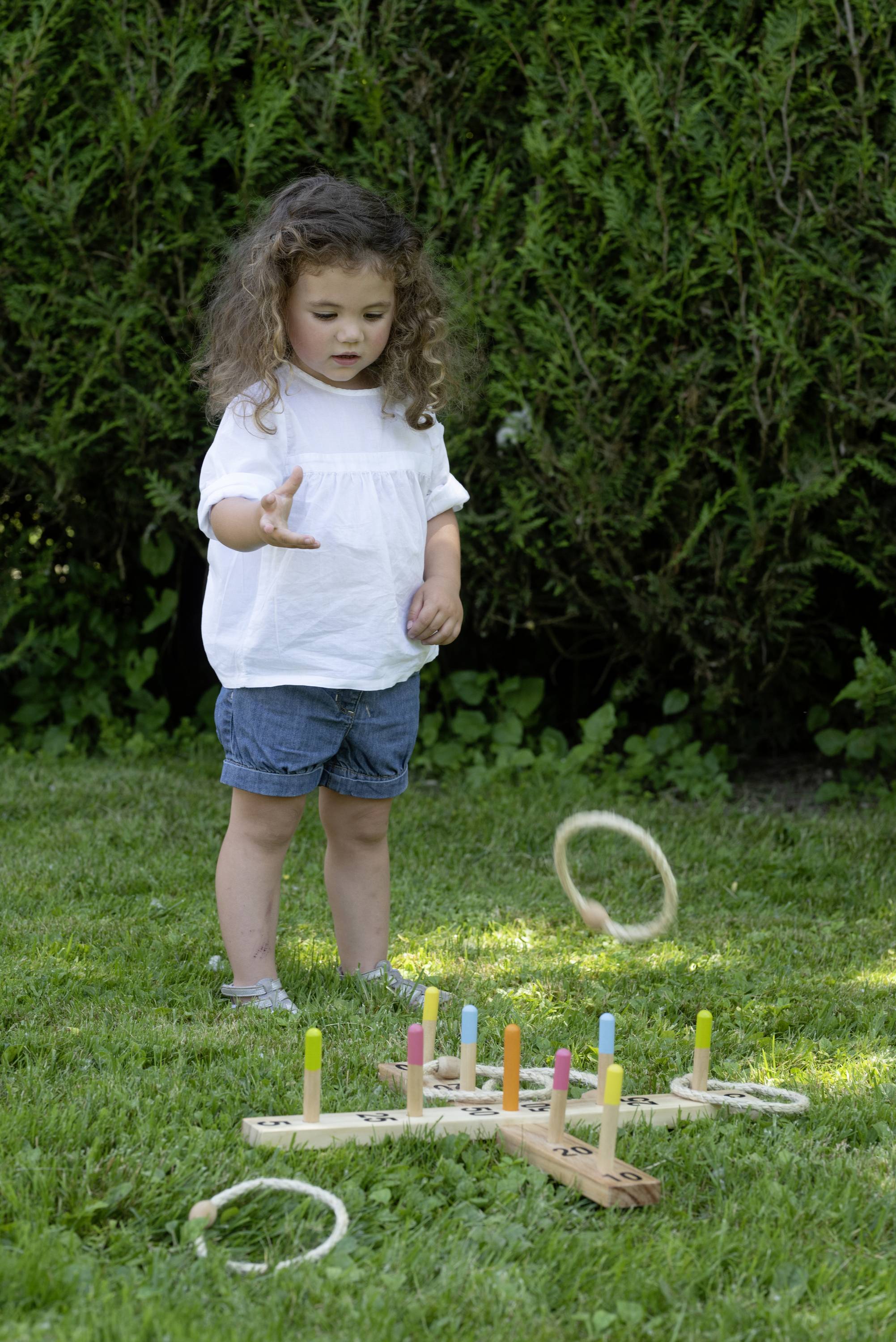 Ein Kind wirft Ringe auf bunte Holzstäbe in einem Garten. Das Spiel fördert die Geschicklichkeit und Zielsicherheit.