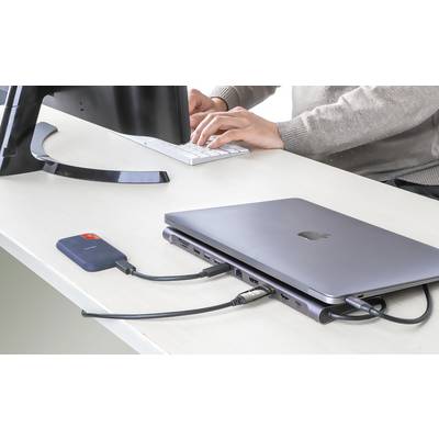 Ein Laptop auf einem Schreibtisch ist mit einem externen Speichergerät und einem Monitor verbunden. Eine Person tippt auf einer Tastatur.