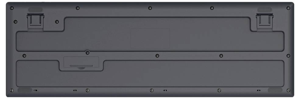 Rückseite einer schwarzen Tastatur mit sichtbaren Rillen und Befestigungsschrauben. Oben sind zwei ausklappbare Stützen erkennbar.