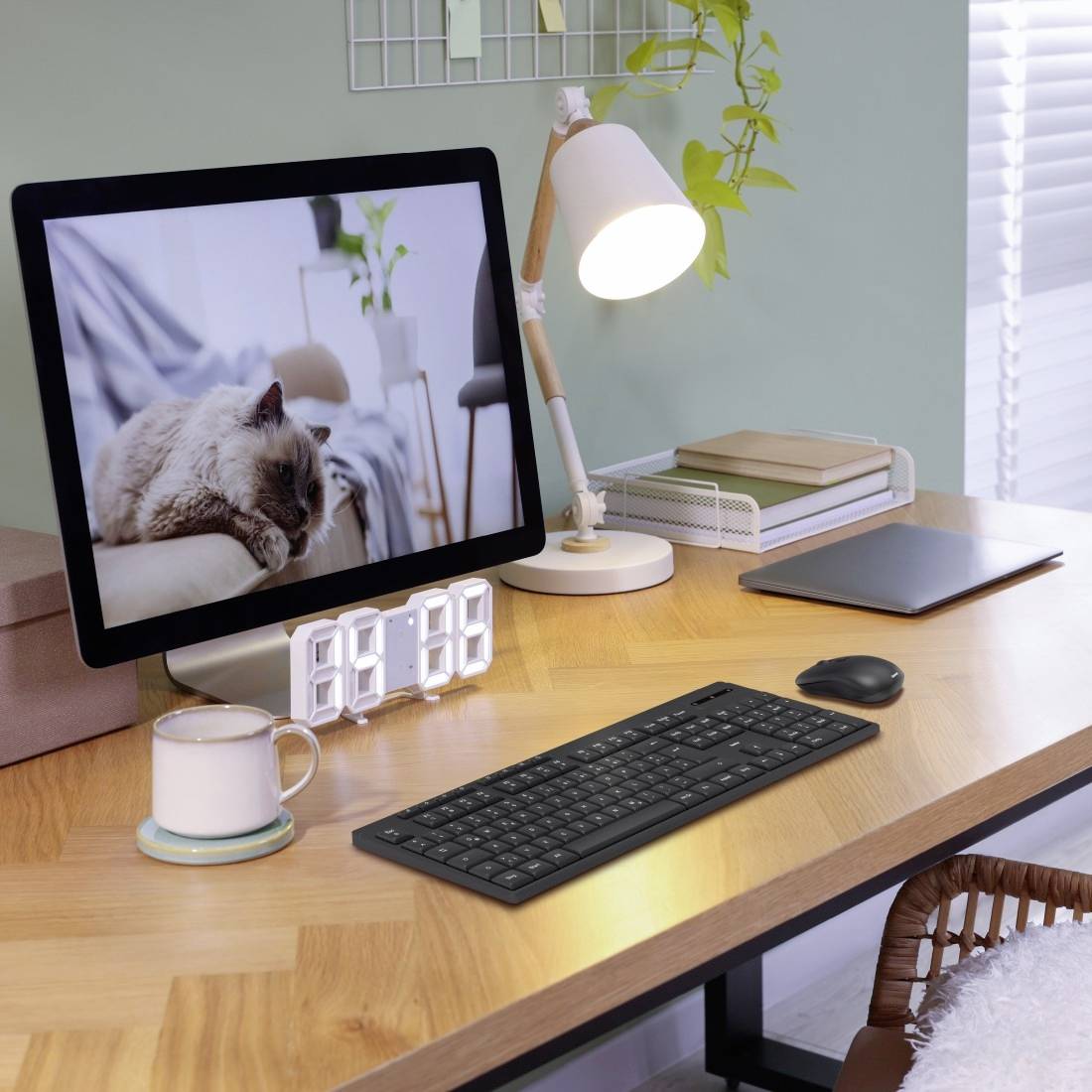 Ein Schreibtisch mit einem Computerbildschirm, der eine Katze zeigt. Daneben stehen eine Lampe, eine Tasse und eine Tastatur.