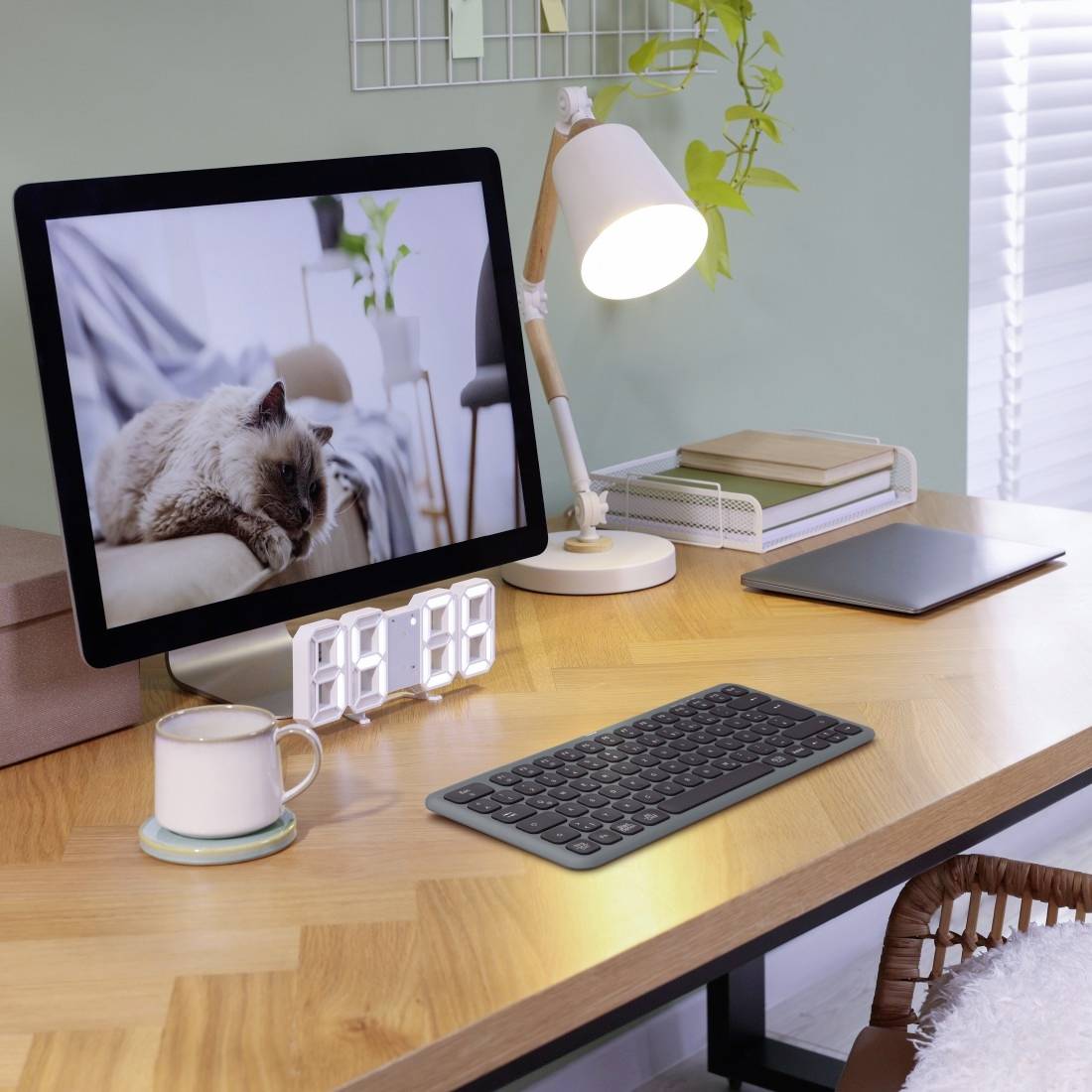 Ein Schreibtisch mit einem Monitor, der eine Katze auf einem Sofa zeigt. Daneben stehen eine Lampe, Tasse, Tastatur und Notizbuch.
