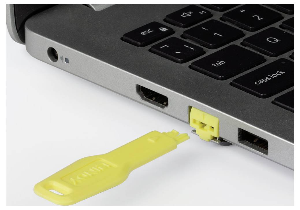 Gelber USB-Stick wird in einen USB-Anschluss eines Laptops auf einer weißen Oberfläche eingesteckt.