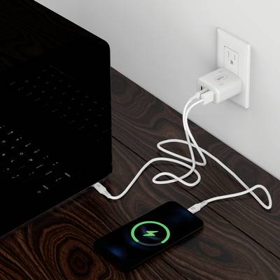 Ein Smartphone wird auf einem Tisch kabellos aufgeladen. Ein Laptop ist daneben zu sehen. Ein Ladegerät ist in der Wandsteckdose.