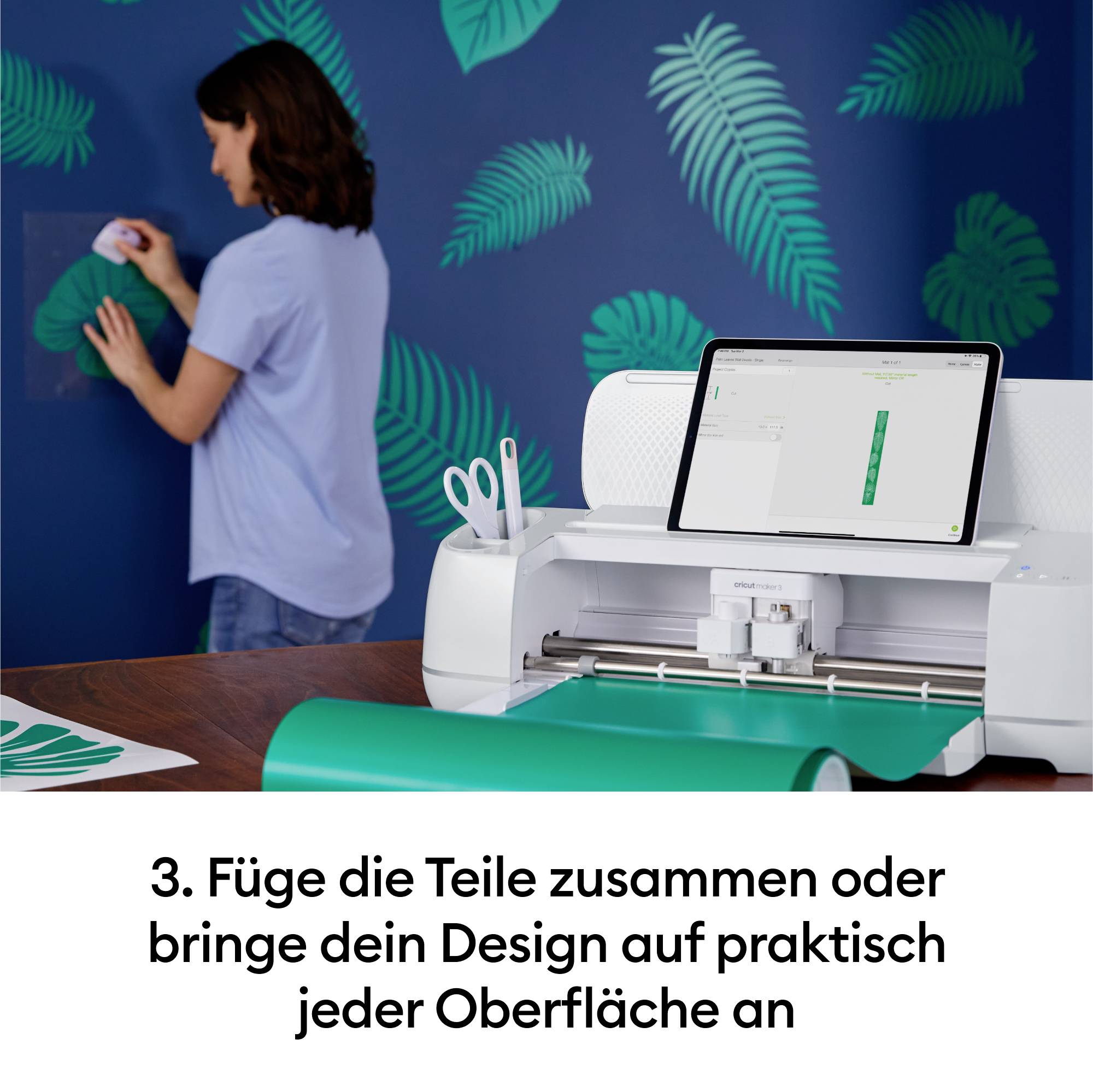 Eine Person arbeitet an einer Wand mit Blattmustern. Vor ihr steht ein Schneideplotter mit einem Tablet darauf. Text: '3. Füge die Teile zusammen oder bringe dein Design auf praktisch jeder Oberfläche an'.