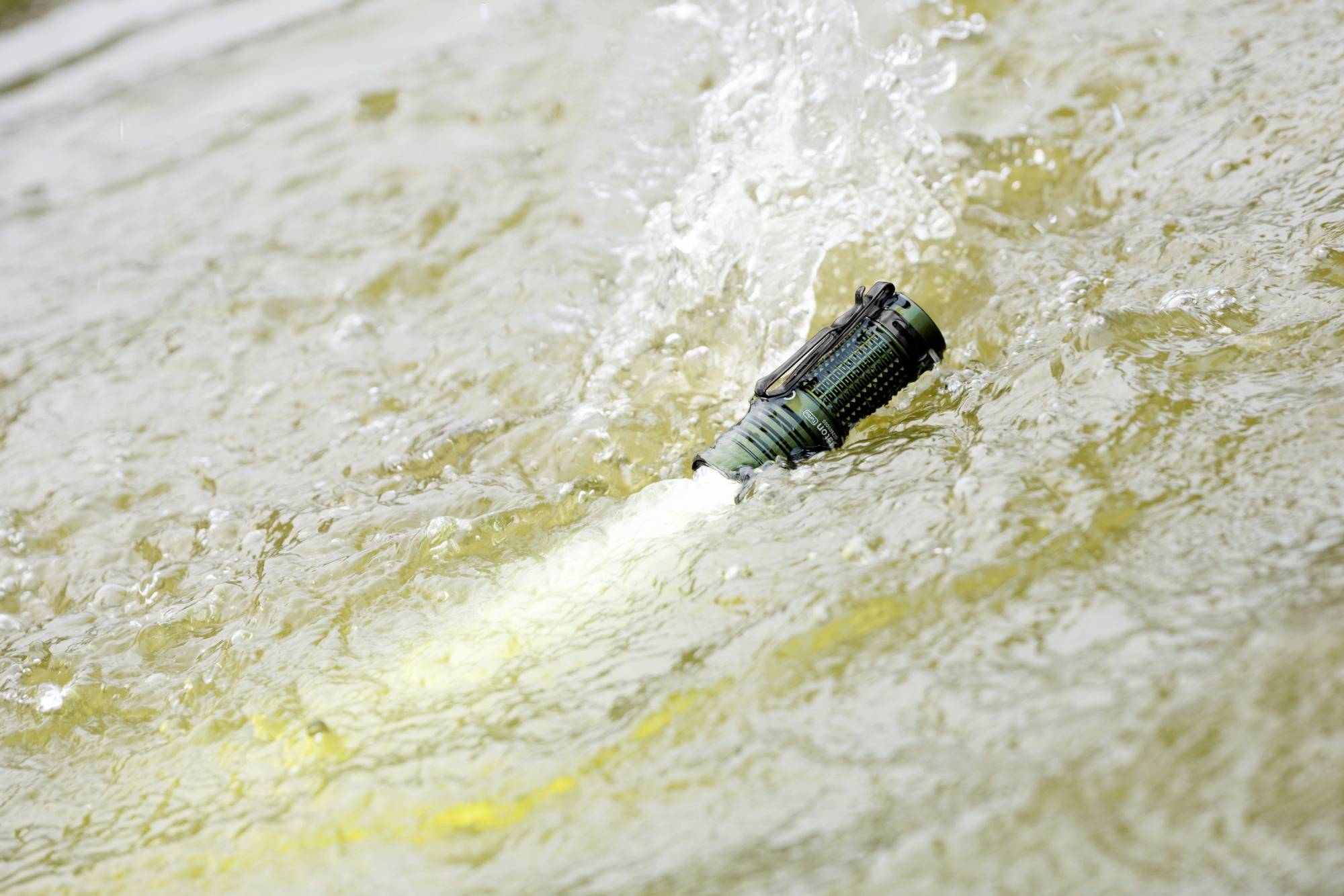 Eine grüne Taschenlampe ist eingeschaltet und schwimmt auf der Wasseroberfläche, wobei sie leuchtet und Wellen verursacht.