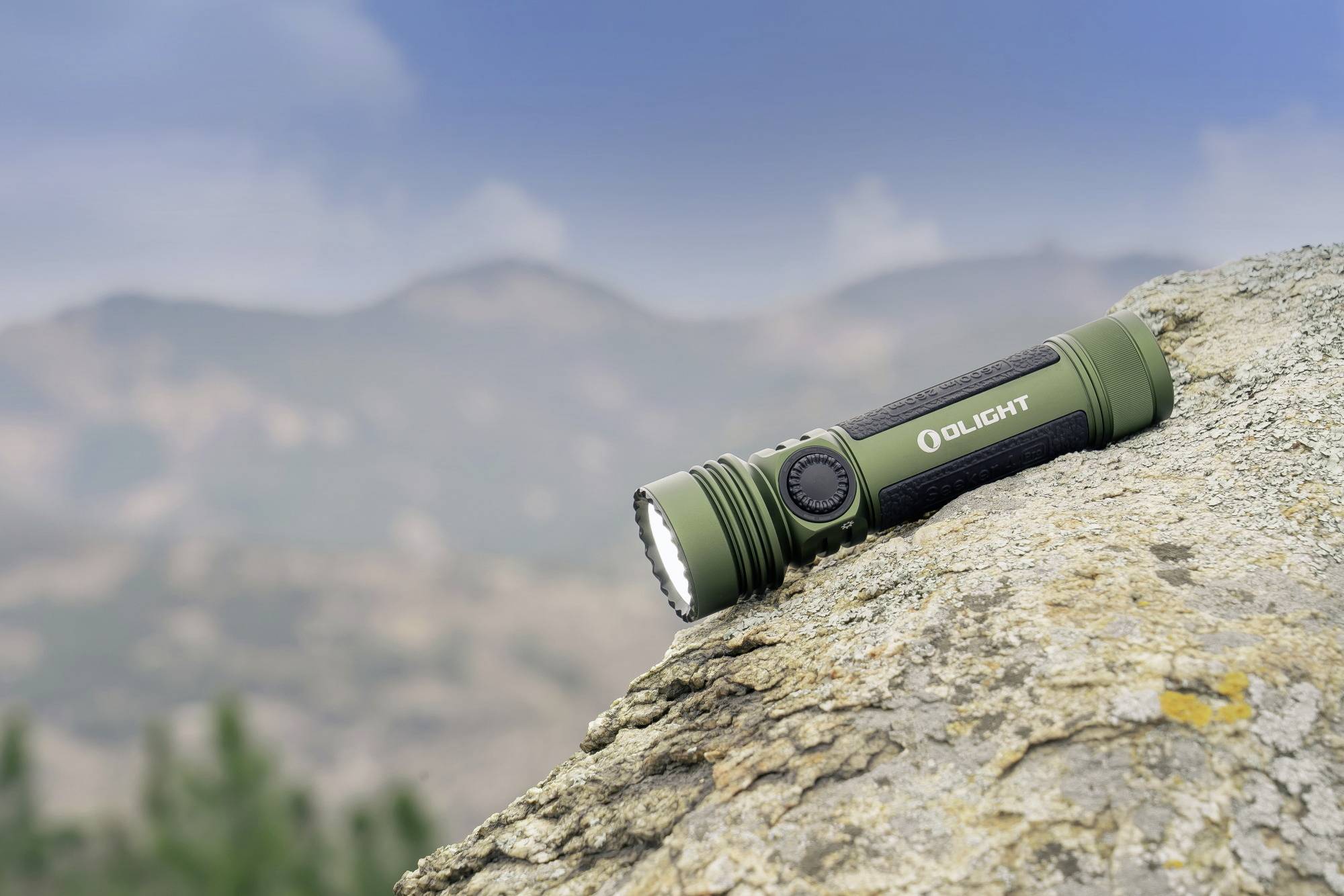 Eine grüne Taschenlampe liegt auf einem Felsen mit verschwommenen Bergen im Hintergrund, bei Tageslicht fotografiert.