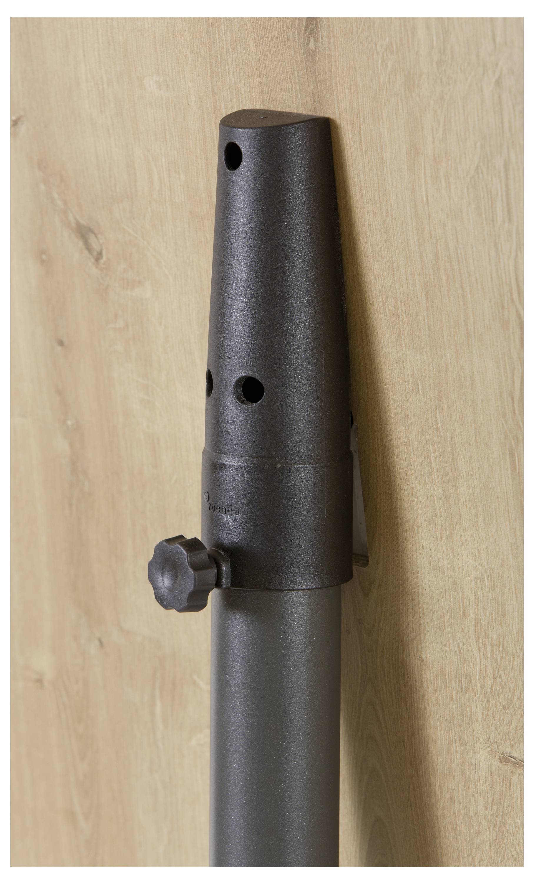 Schwarzes, zylinderförmiges Objekt mit Drehknopf vor einer Holzoberfläche. Es scheint sich um ein verstellbares Möbel- oder Gerätebein zu handeln.