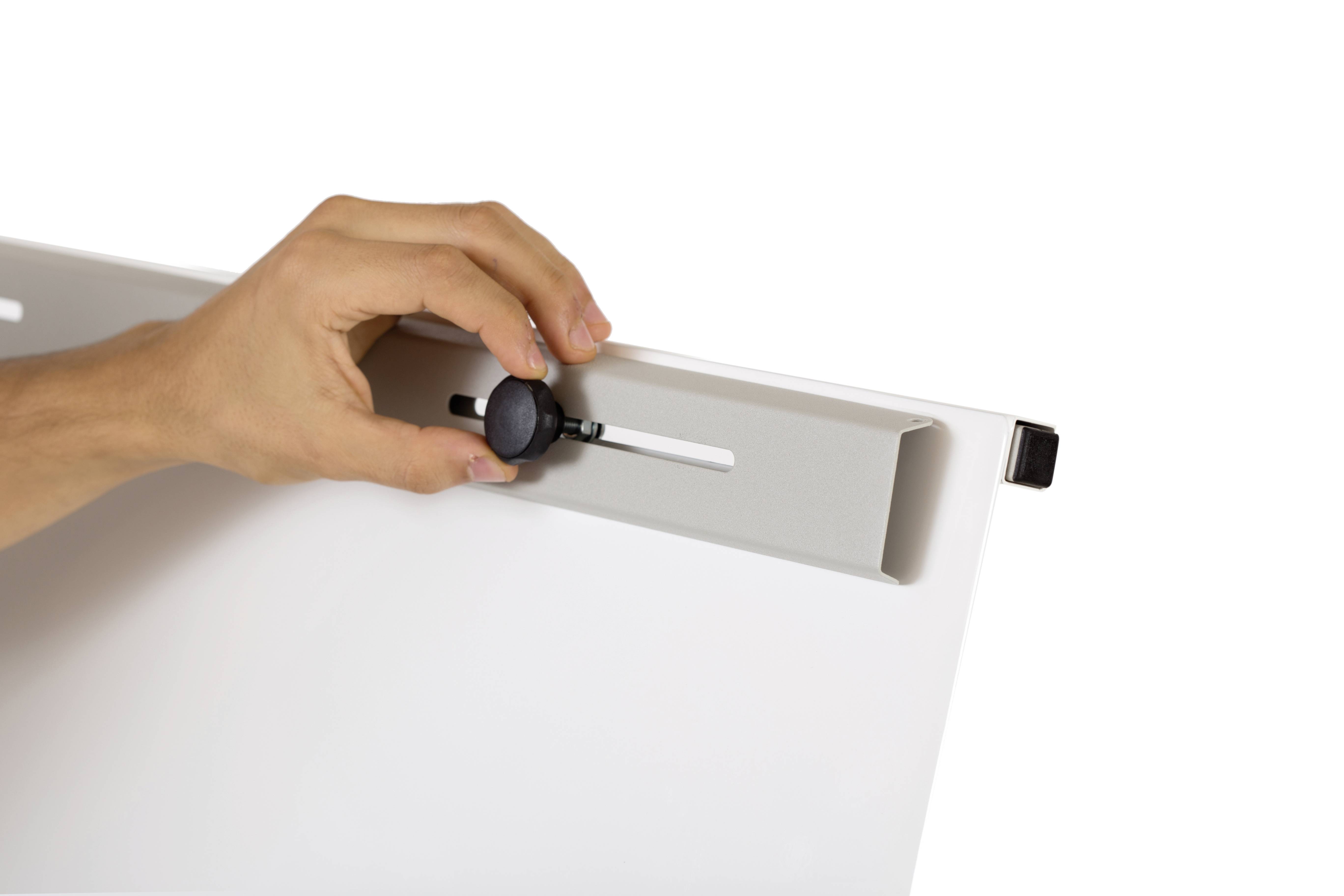 Eine Hand stellt einen schwarzen Knopf auf einem weißen Brett ein, wahrscheinlich zur Justierung oder Befestigung.