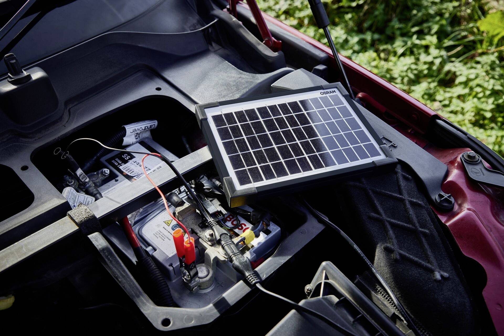 Ein Solarladegerät lädt die Autobatterie eines offenen Motorraums, das von Sonnenlicht beschienen wird.