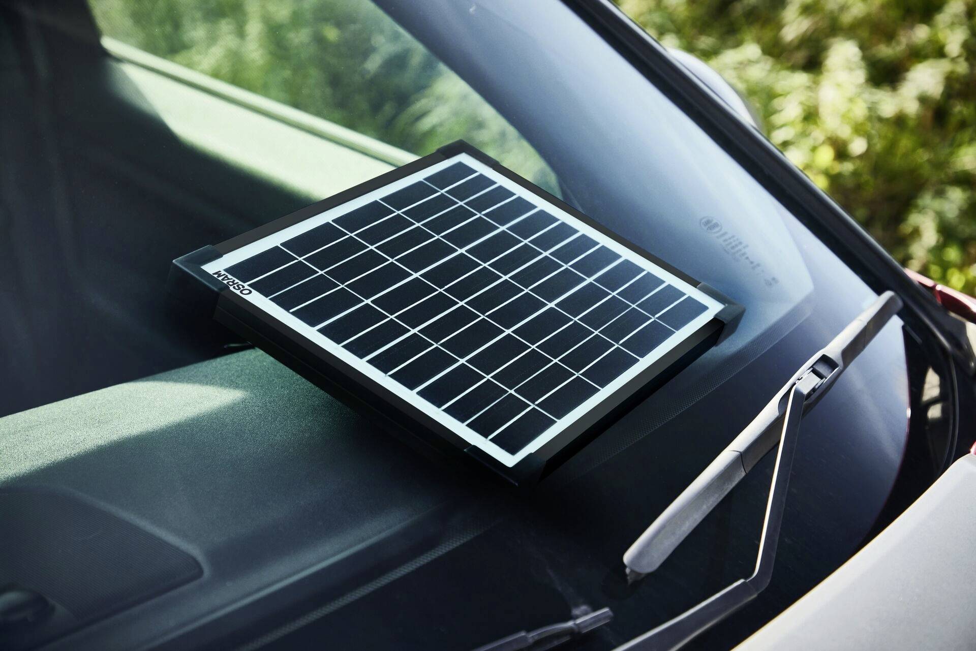 Ein kleines Solarpanel liegt auf dem Armaturenbrett eines Autos, positioniert hinter der Windschutzscheibe, um Sonnenenergie zu sammeln.