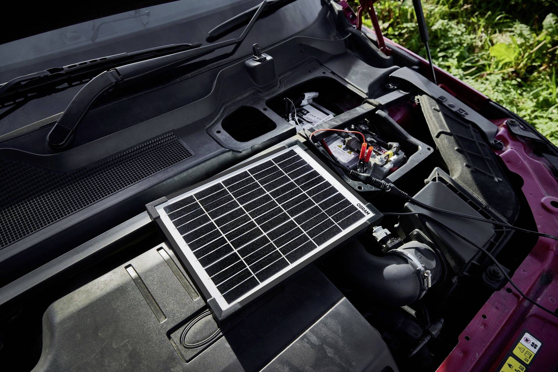 Ein Solarpanel ist am Motorraum eines Autos befestigt, um die Autobatterie aufzuladen. Sonnenlicht fällt auf das Solarpanel.