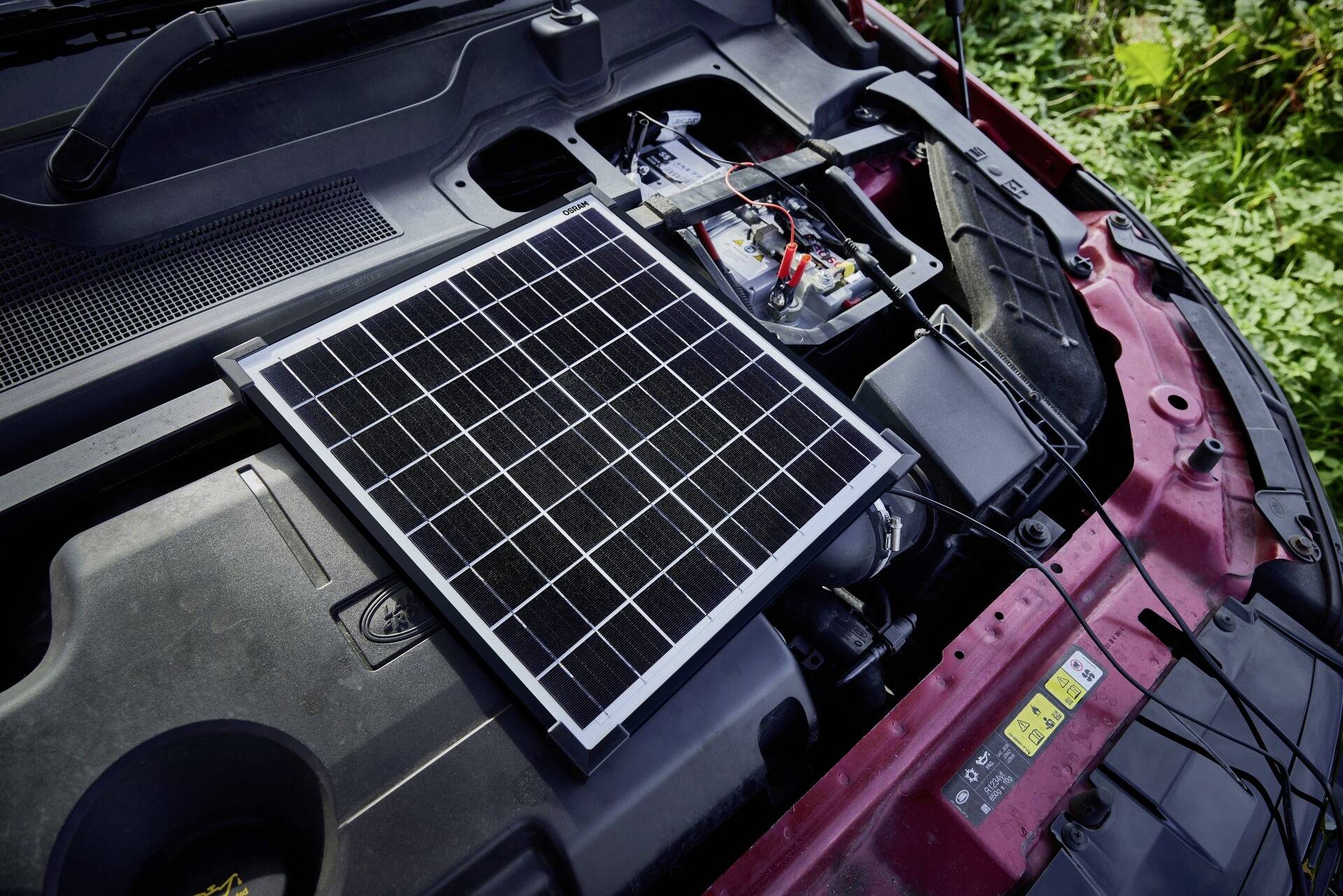 Ein Solarpanel liegt auf dem Motor eines Autos und lädt die Autobatterie.