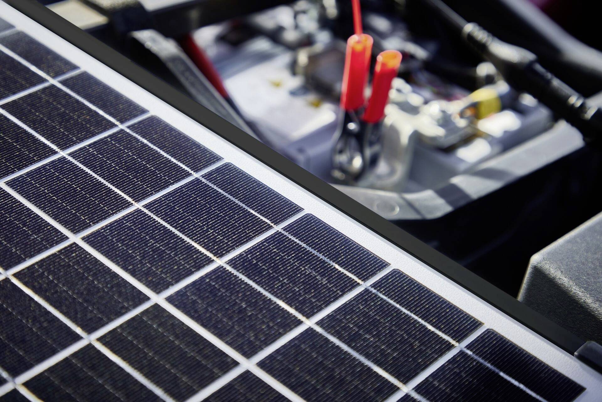 'Solarpanel wird an Autobatterie angeschlossen, um Aufladen zu demonstrieren. Nahaufnahme zeigt Solarpanel und Klemmen auf der Batterie.'
