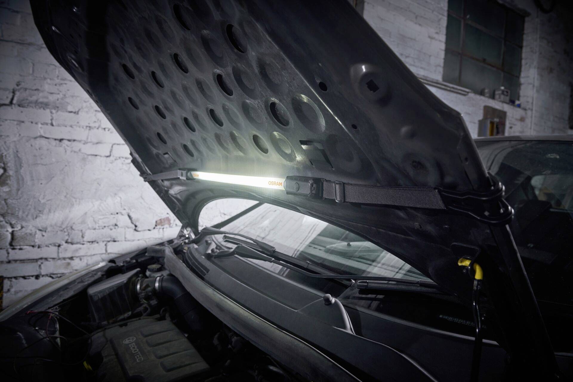 Autowerkstatt: Eine Motorhaube ist geöffnet und eine Lampe beleuchtet den Motorraum eines Fahrzeugs, um Reparaturen zu erleichtern.