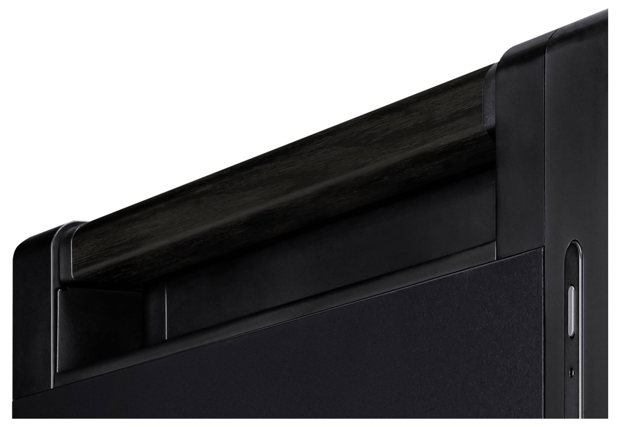 Schwarzer Metallrahmen mit horizontalem Träger auf dunklem Hintergrund. Oberer Teil eines Möbelstücks oder Geräts sichtbar.