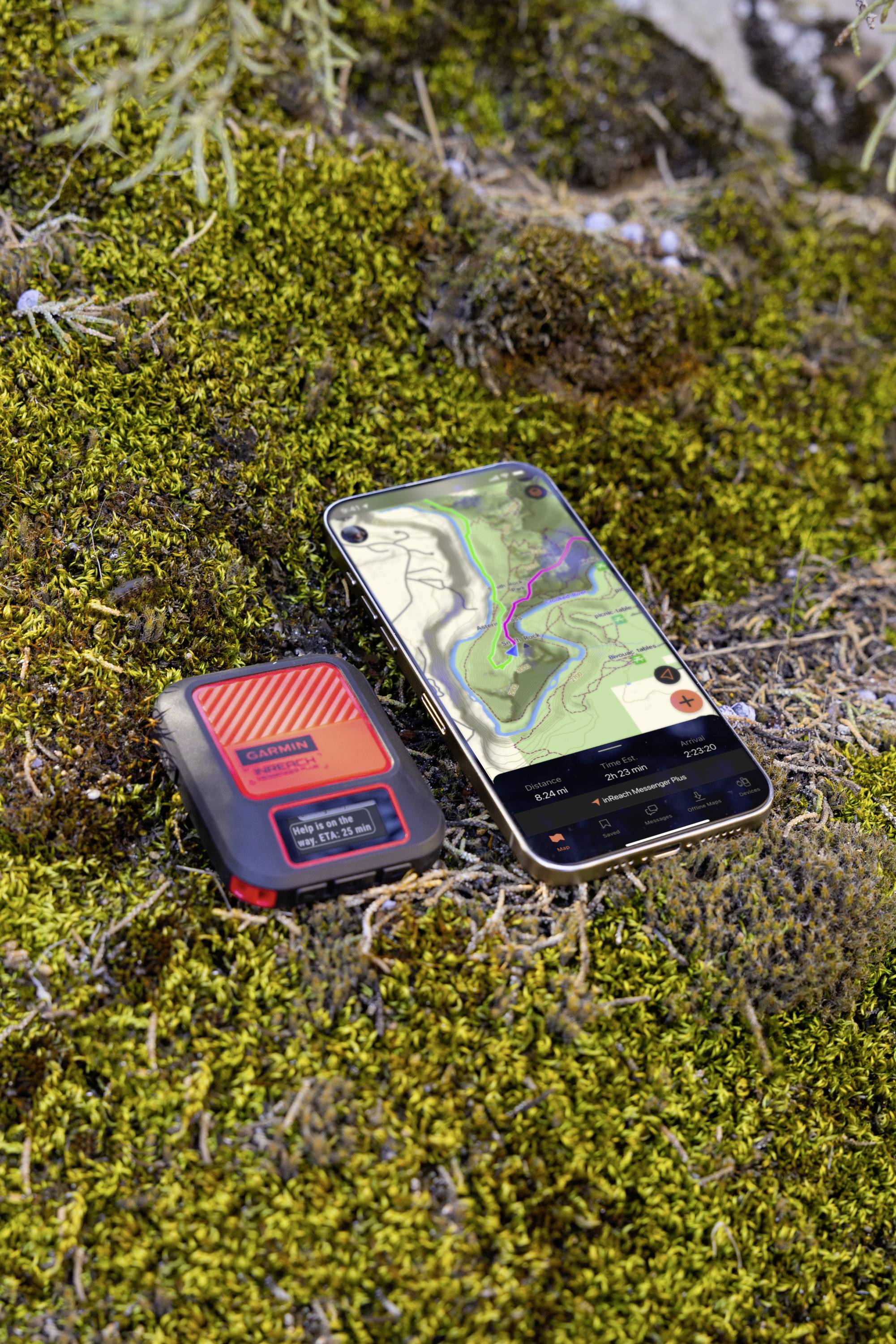 Ein Smartphone mit geöffneter Karten-App und ein kompaktes Outdoor-Gerät liegen auf moosbedecktem Boden.