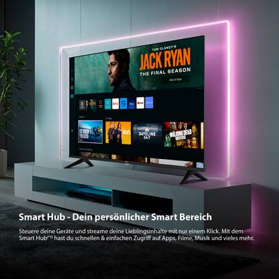 Ein Fernseher, der auf einem modernen weißen Ständer eine Smart-Hub-Schnittstelle anzeigt. Der Bildschirm zeigt verschiedene Streaming-Optionen mit hervorgehobenem 'Jack Ryan: The Final Season'. Rosa LED-Leuchten rahmen den Fernseher ein.