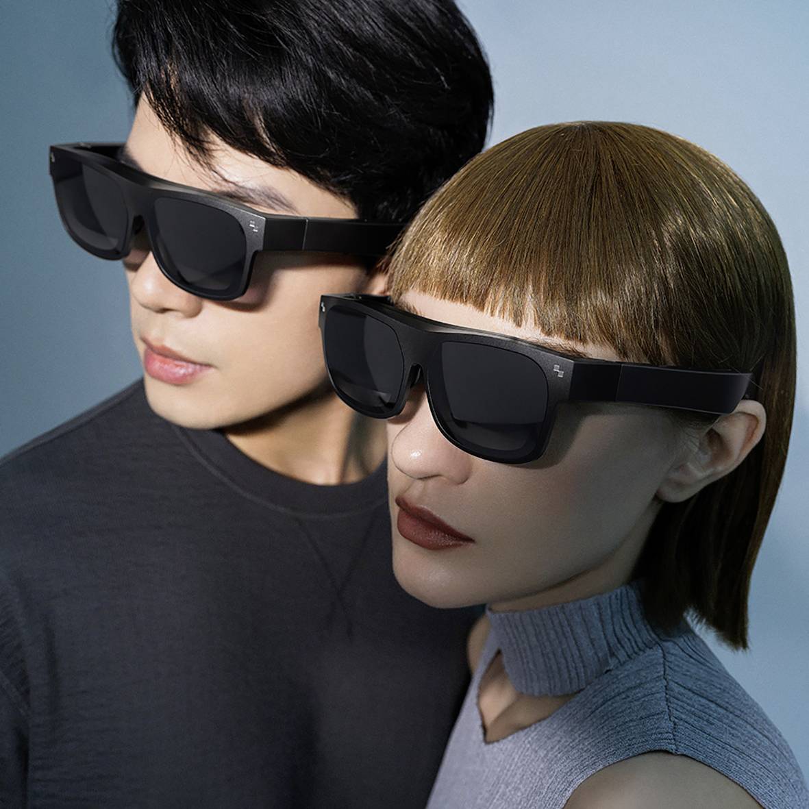 Zwei Personen tragen moderne, schwarze Virtual-Reality-Brillen. Sie schauen in dieselbe Richtung. Der Hintergrund ist neutral gehalten.