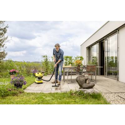 Ein Mann reinigt eine Terrasse mit einem Hochdruckreiniger, umgeben von Pflanzen und Gartenmöbeln. Der Himmel ist bewölkt.