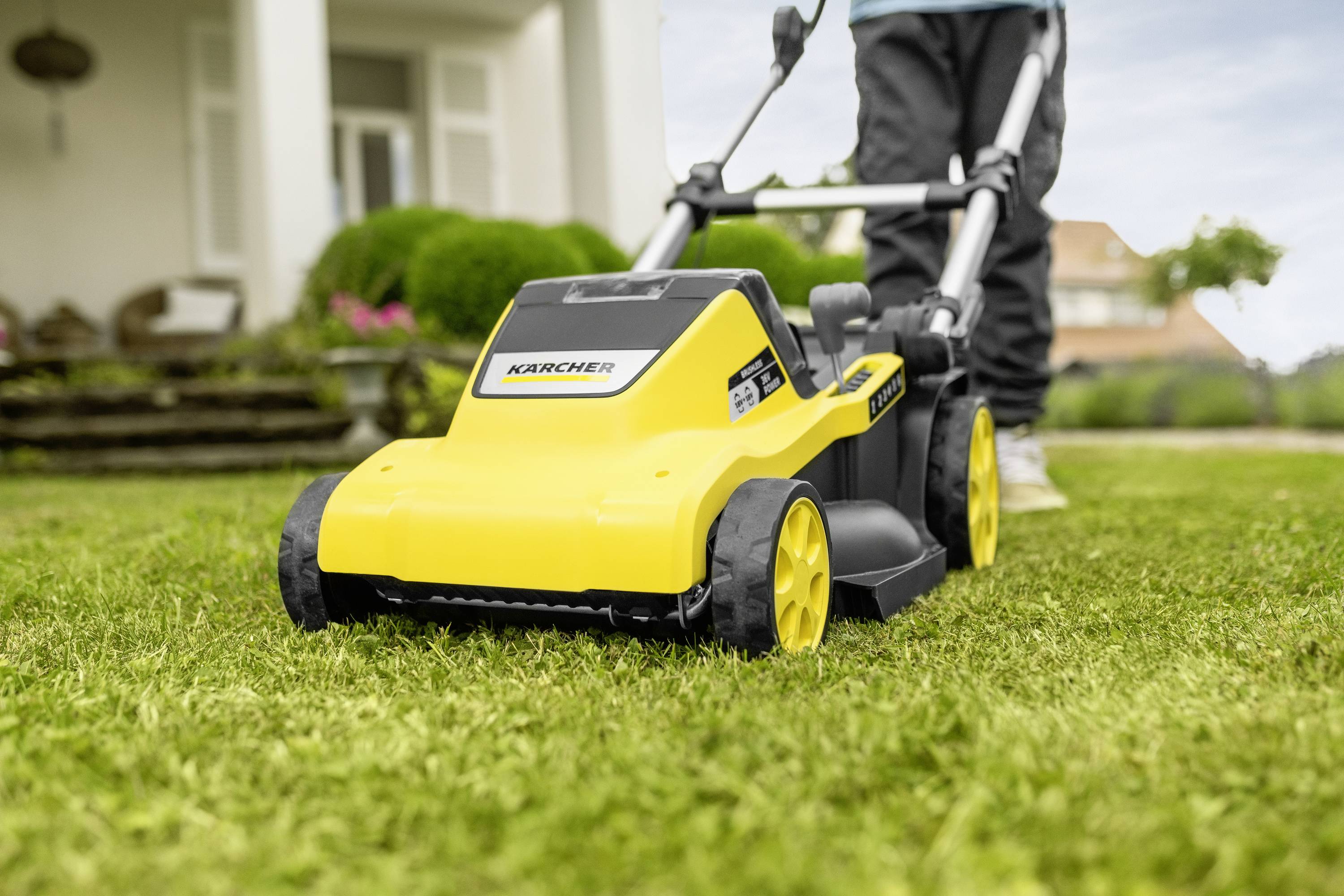Eine Person mäht den Rasen mit einem gelben Rasenmäher in einem Garten vor einem Haus.