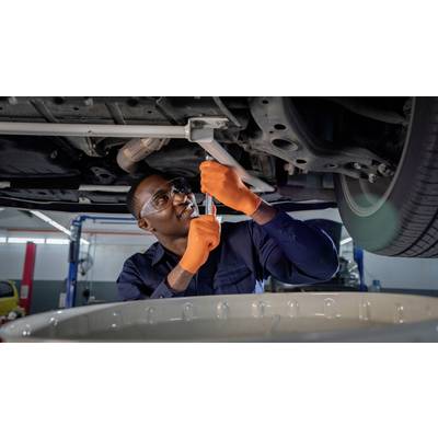 Ein Mechaniker mit Schutzbrille und orangefarbenen Handschuhen repariert ein Fahrzeug von unten in einer Werkstatt.