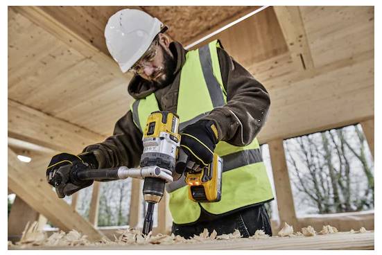 Ein Bauarbeiter in einer Warnweste und mit Schutzhelm verwendet einen Akkuschrauber auf einer Holzoberfläche in einem Gebäude im Bau.