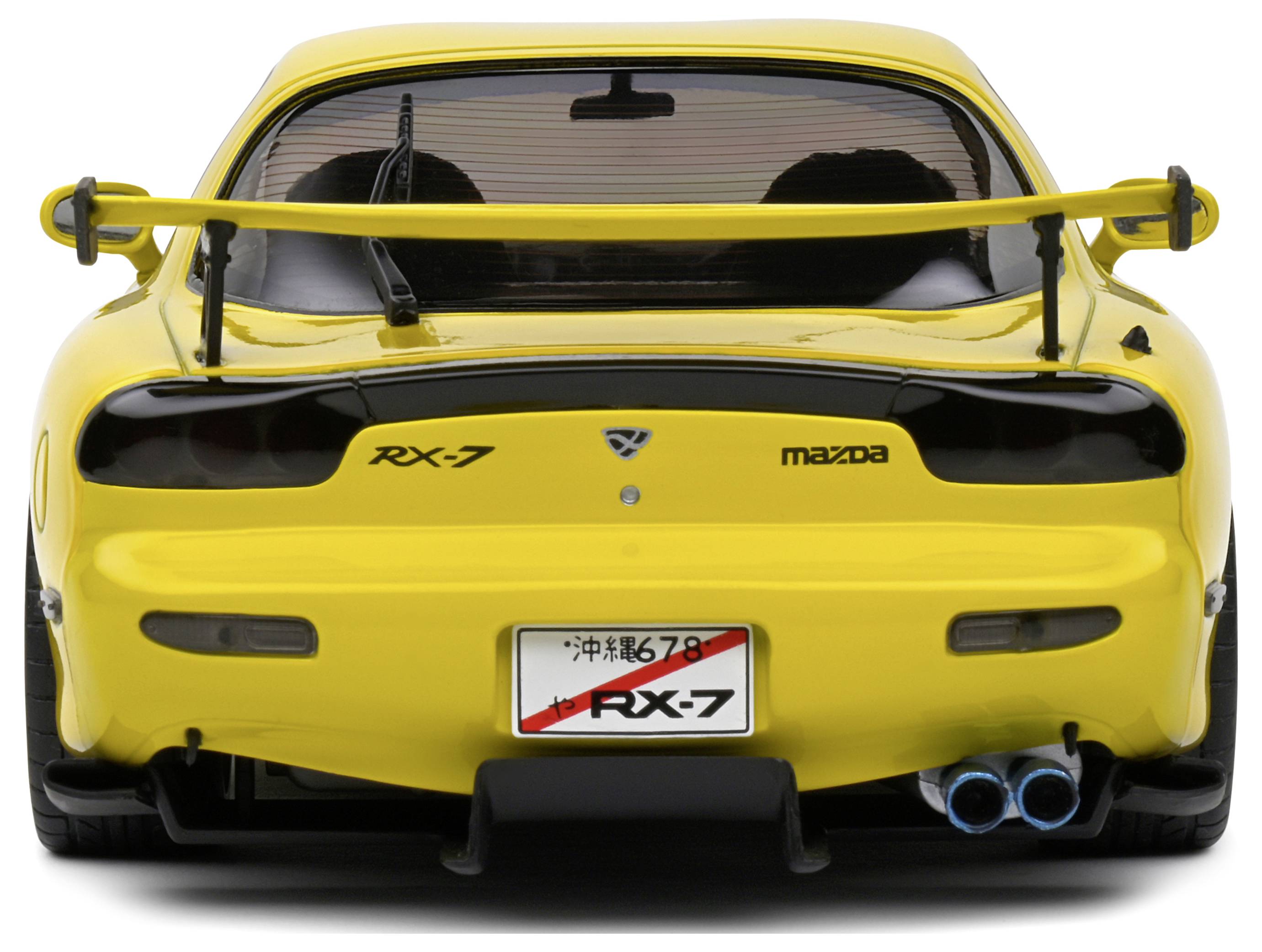 Gelber Sportwagen von hinten, Modell Mazda RX-7, mit Heckspoiler und Doppelrohrauspuff, auf einem Parkplatz stehend.