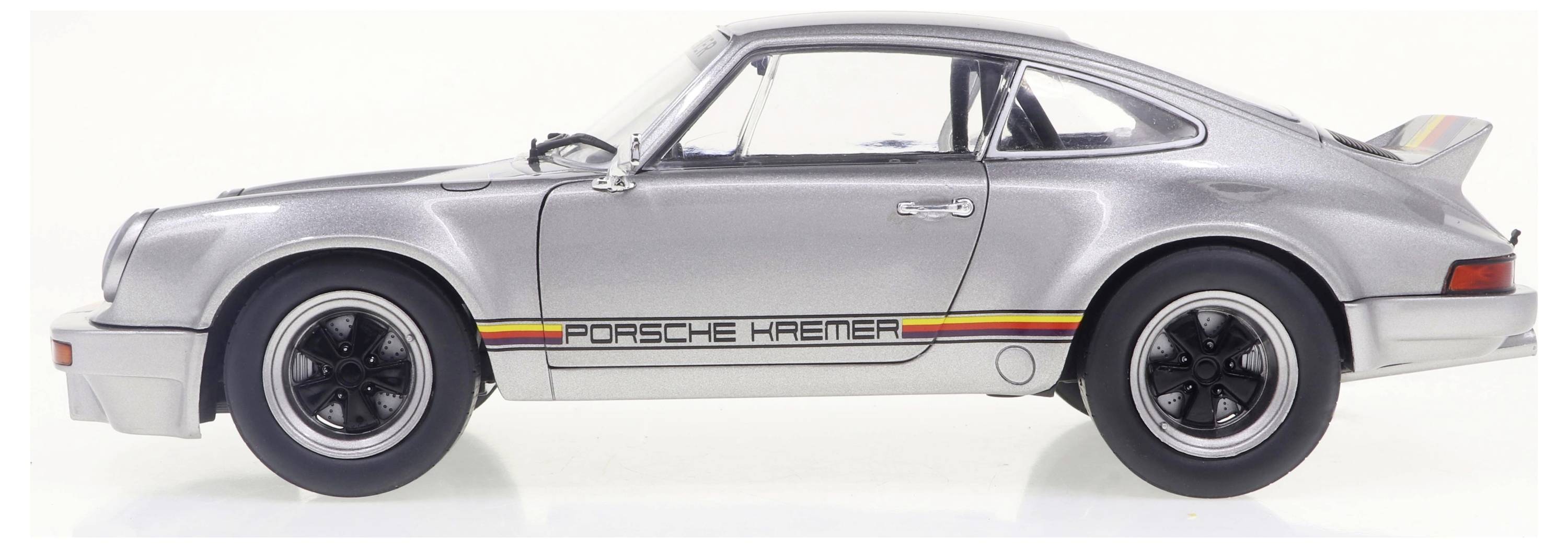 Ein silberner Sportwagen mit der Aufschrift 'Porsche Kremer' an der Seite. Fahrer- und Beifahrertür sowie Heckspoiler sichtbar.