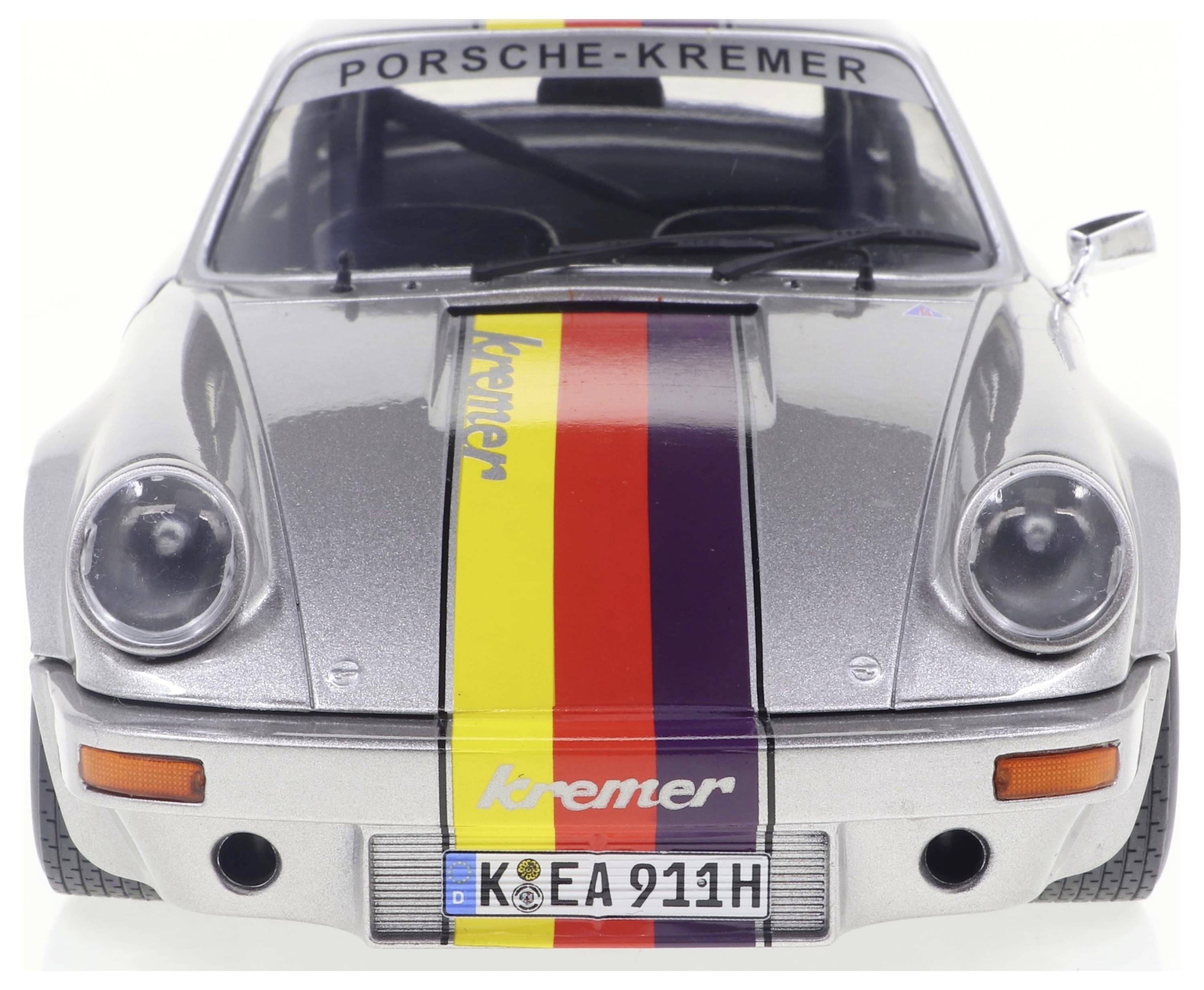 Silberner Porsche mit Kremer-Streifen in Gelb, Rot und Schwarz. Nummernschild: 'K-EA 911H'. Vorderansicht zeigt Scheinwerfer und Kühlergrill.