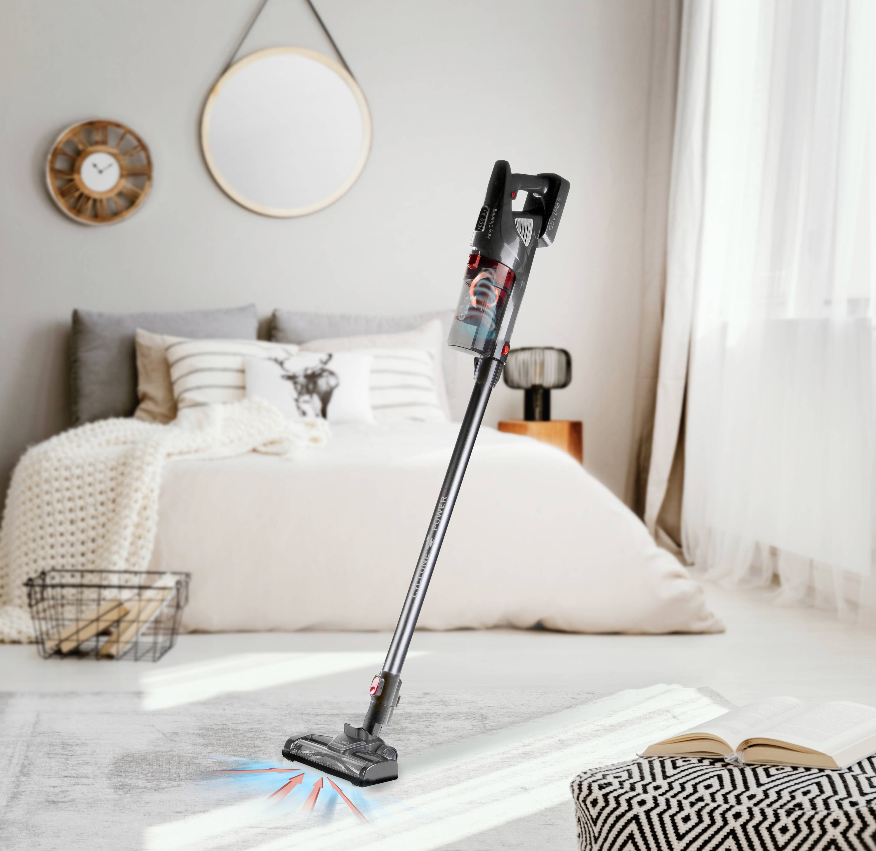 Kabelloser Staubsauger auf hellen Teppich, modernes Wohnzimmer im Hintergrund. Spiegel, Uhr und Sofa mit Kissen, Fenster mit Vorhängen.