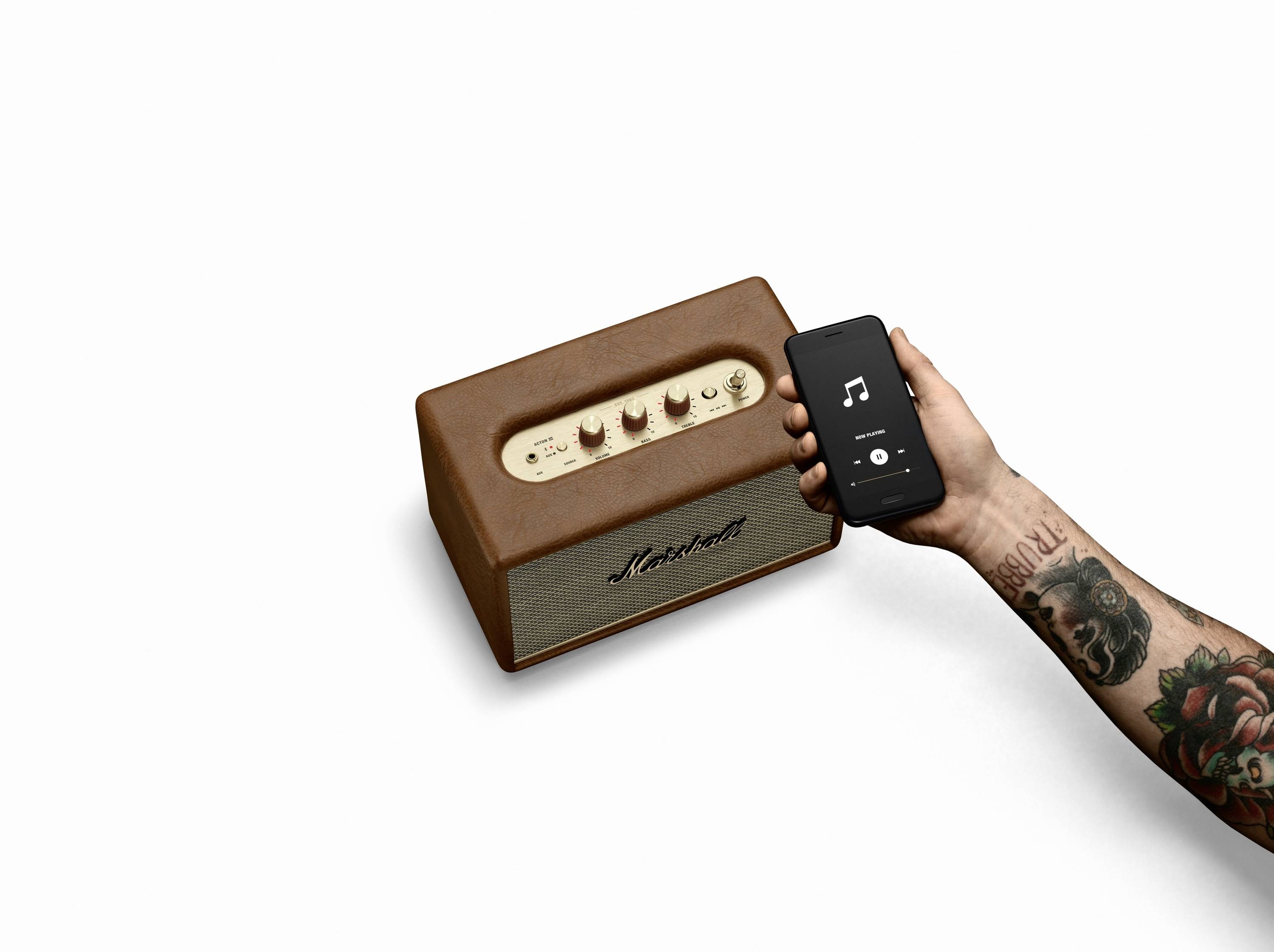 Person hält Smartphone mit Musik-App neben einem braunen Lautsprecher. Der Lautsprecher hat Regler und das Logo 'Marshall'.