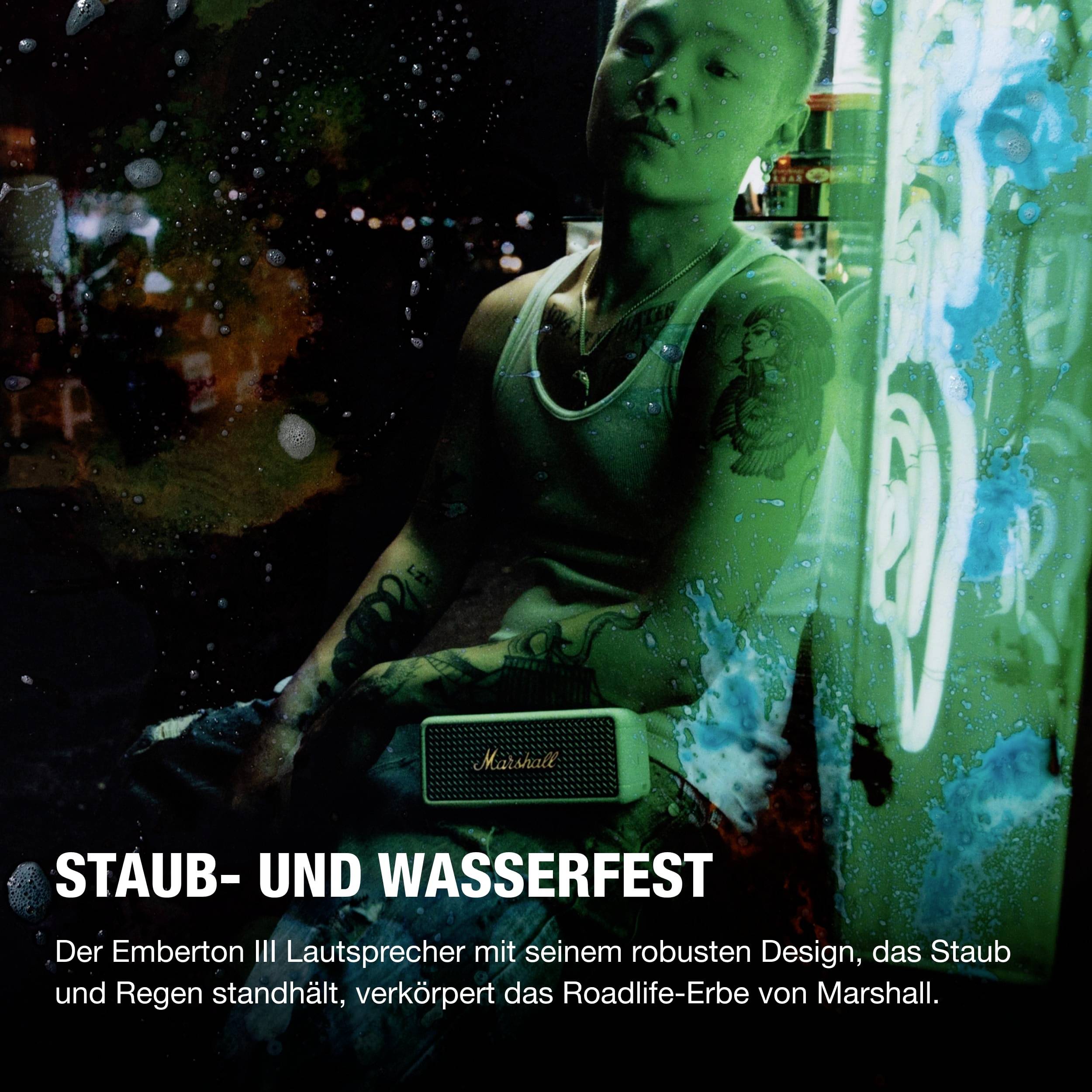 'Ein Mann hält einen Marshall Emberton II Lautsprecher. Hintergrund zeigt Neonlichter. Text: Staub- und wasserfest, Roadlife-Erbe von Marshall.'