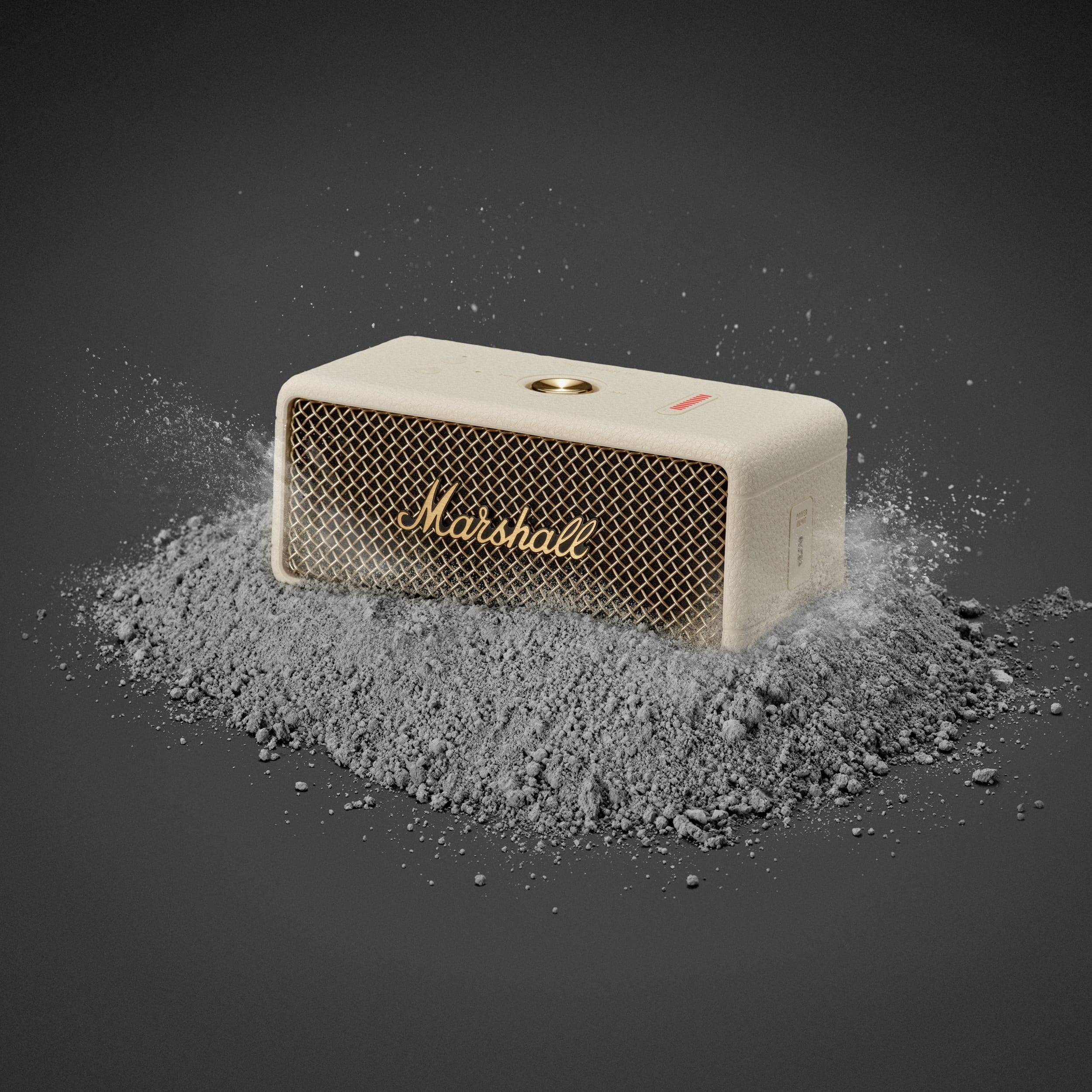 Ein tragbarer Lautsprecher mit dem Aufdruck 'Marshall', platziert auf einem Haufen grauer Asche, vor dunklem Hintergrund.