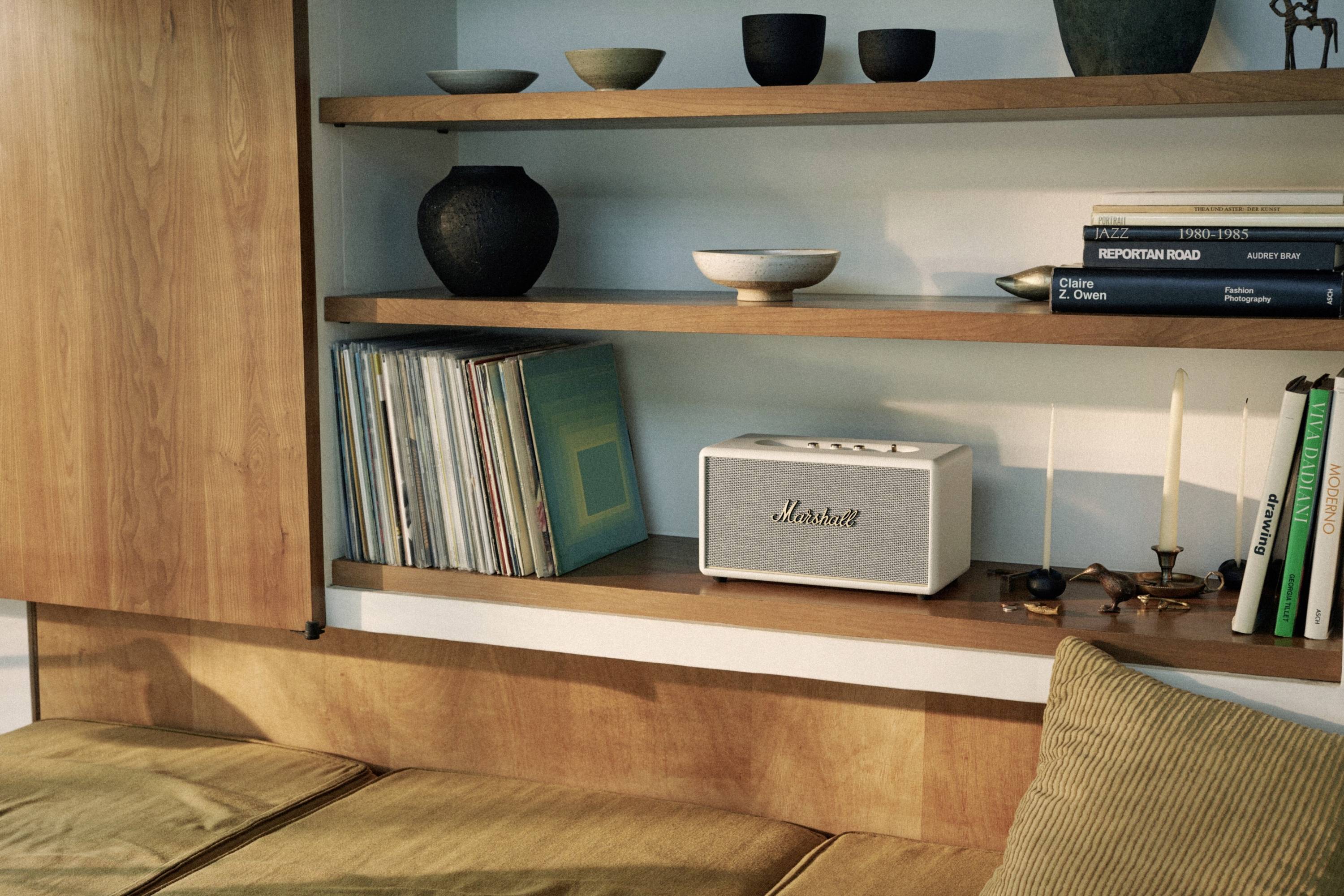 Ein Bücherregal mit Dekorationsartikeln, Schallplatten und einem Lautsprecher. Darunter ein Sofa mit Kissen.