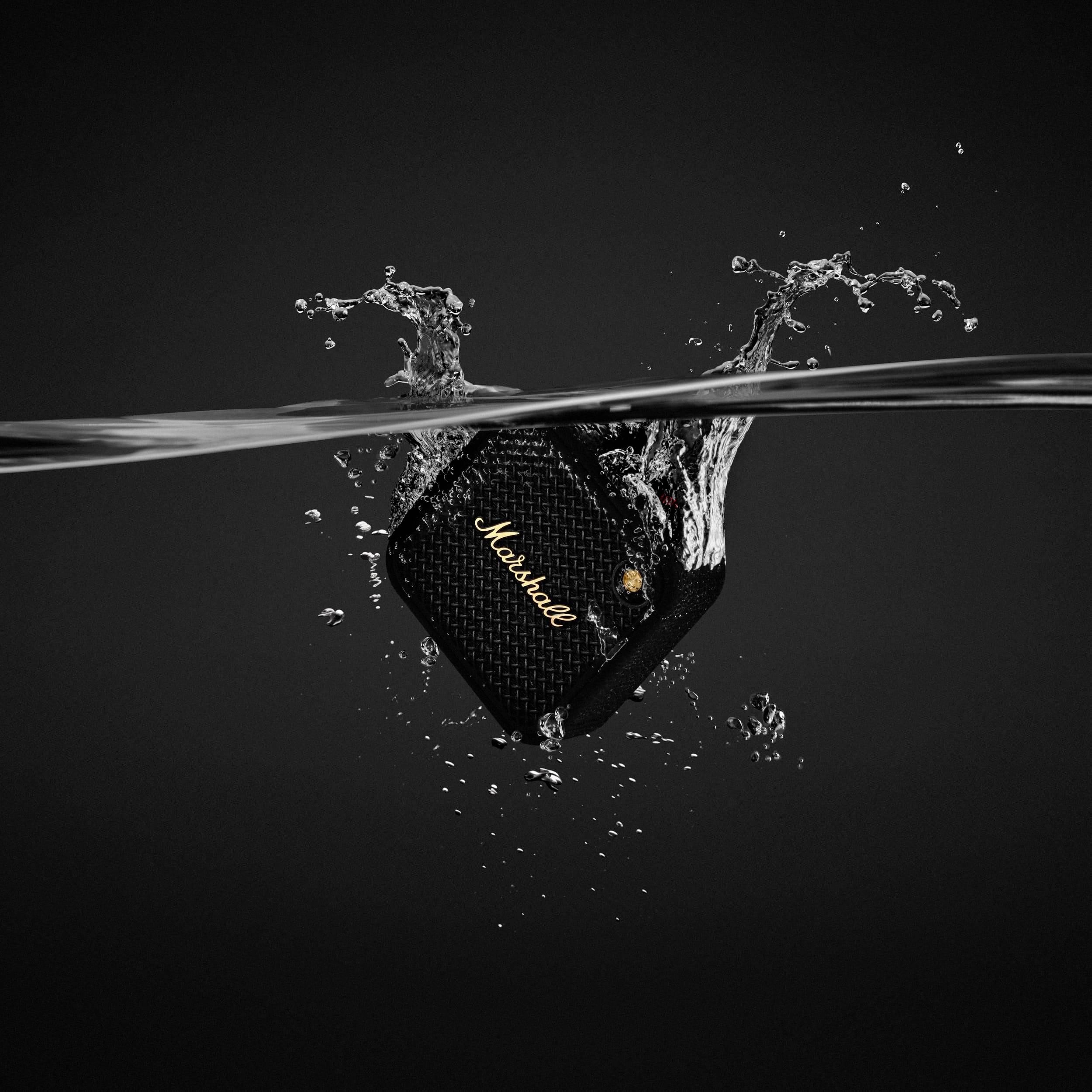 Ein schwarzer Lautsprecher wird in Wasser getaucht, Wasser spritzt nach oben. Der Lautsprecher hat den Markennamen in weißer Schrift.