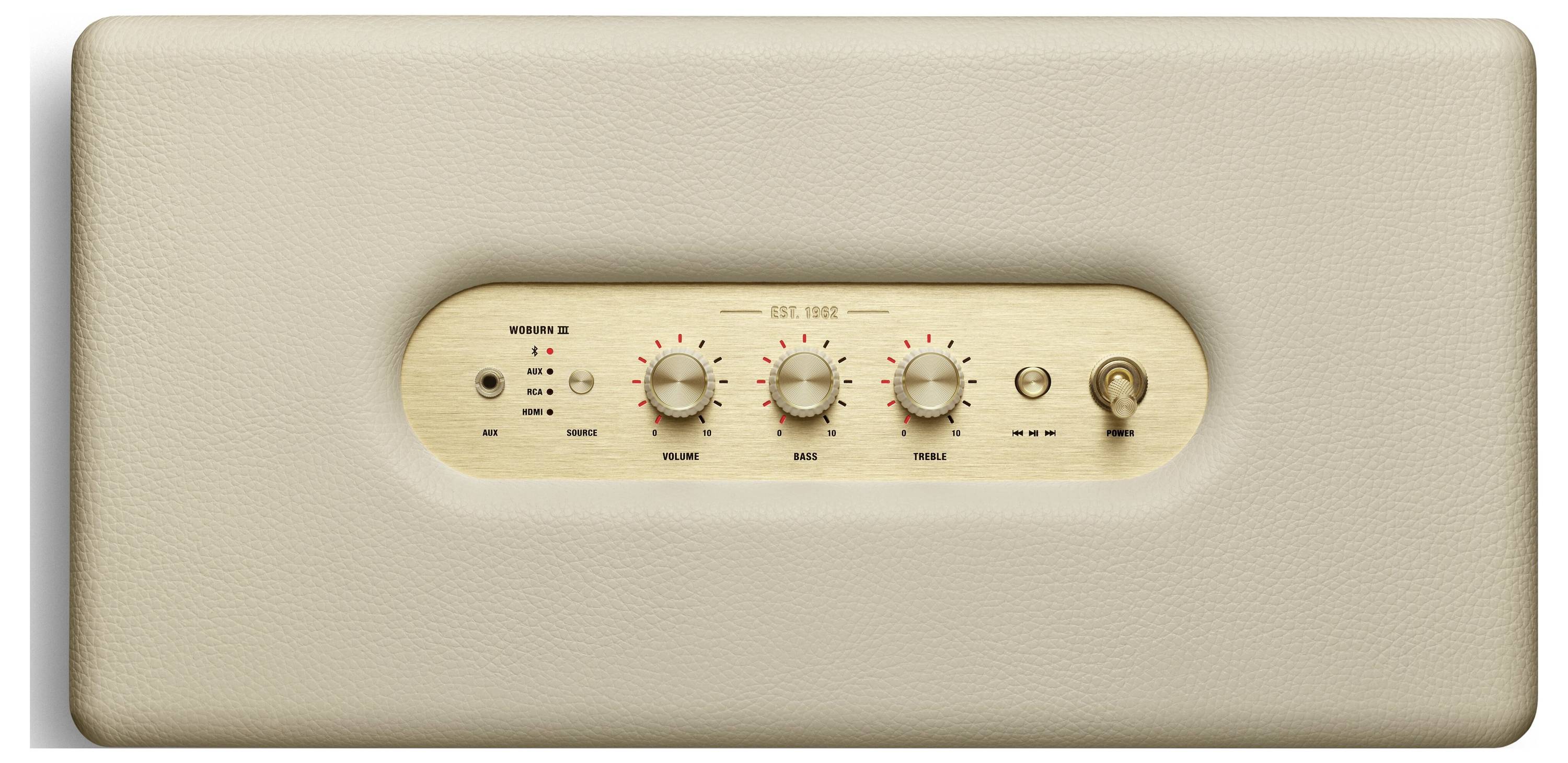 Beige Lautsprecher mit ovalem Bedienfeld. Vier Drehknöpfe für 'Bass', 'Treble', 'Volume' und 'Source', Schalter rechts daneben.