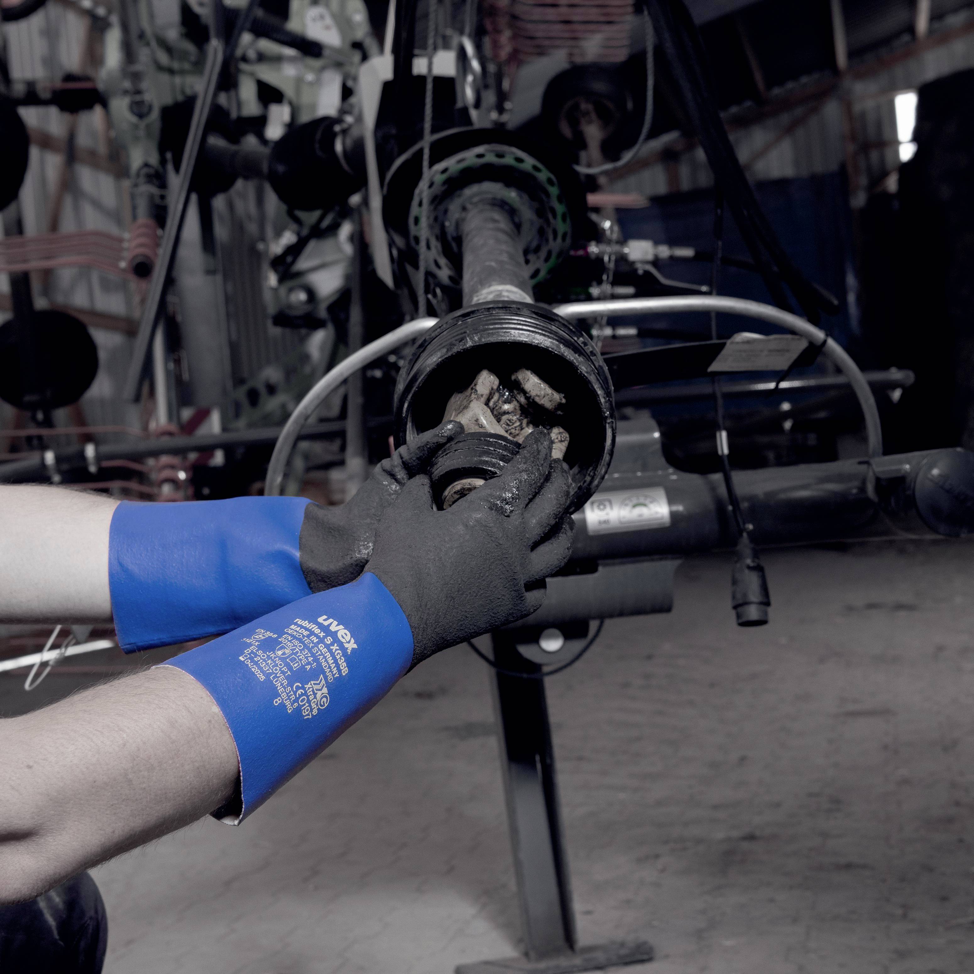 Mechaniker in blauen Handschuhen repariert ein Fahrzeugradlager in einer Werkstatt. Werkzeuge und Hebebühne im Hintergrund.