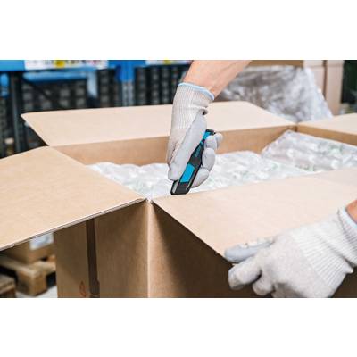 Eine Person öffnet mit einem Cutter in Handschuhen einen großen Karton, der mit Luftpolsterfolie gefüllt ist.