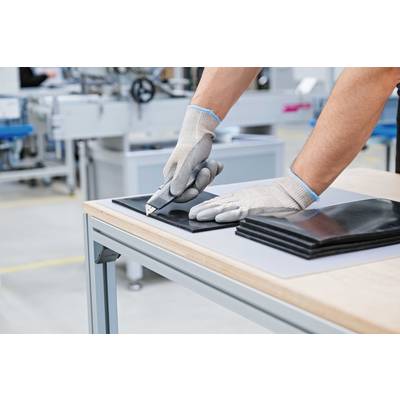 Eine Person schneidet mit einem Cutter Schneidematten, trägt dabei Schutzhandschuhe. Im Hintergrund ist Fabrikwerkzeug zu sehen.