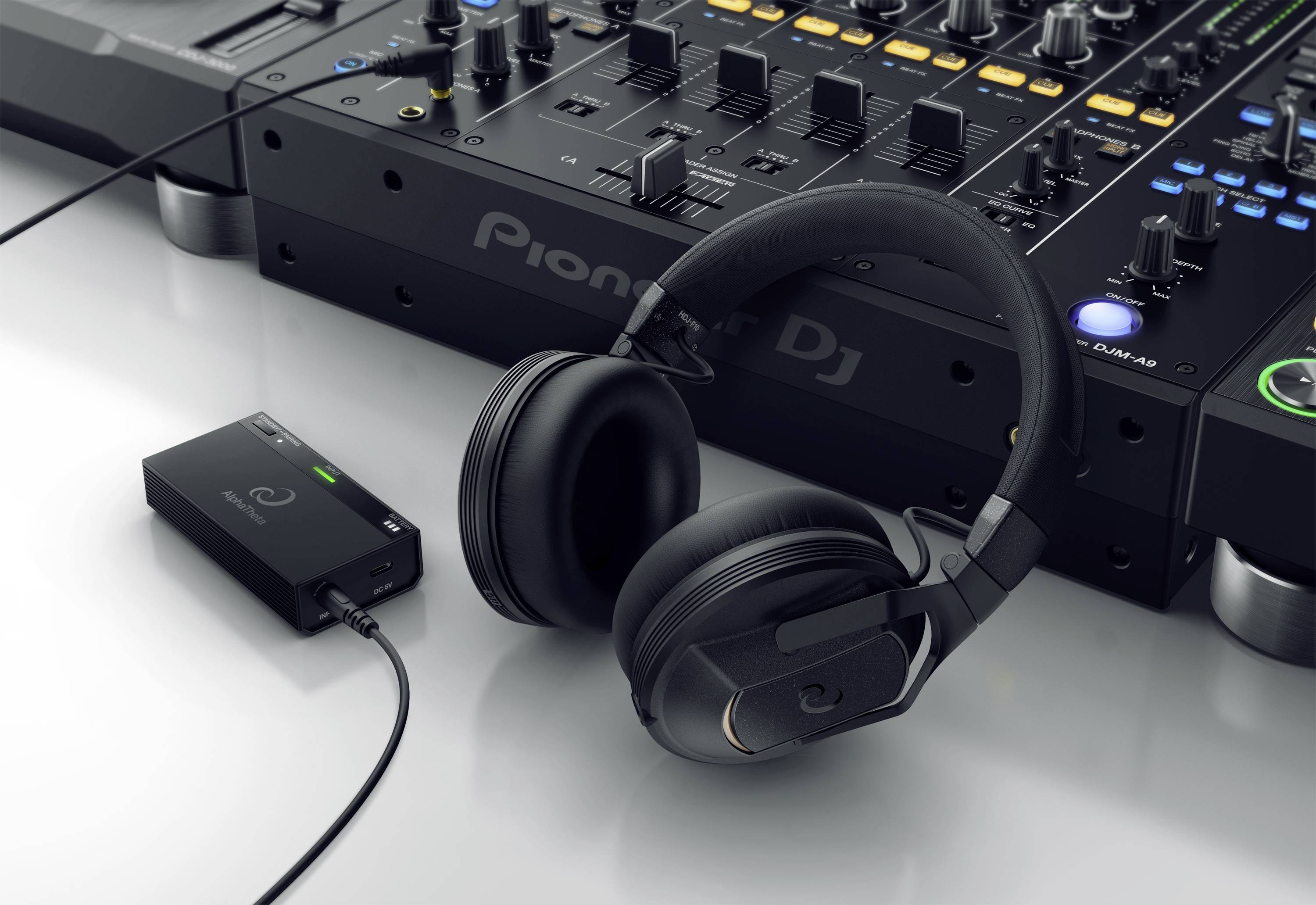 DJ-Ausrüstung mit schwarzen Kopfhörern und Mischpult auf einem Tisch. Ein kleines elektronisches Gerät ist daneben angeschlossen.