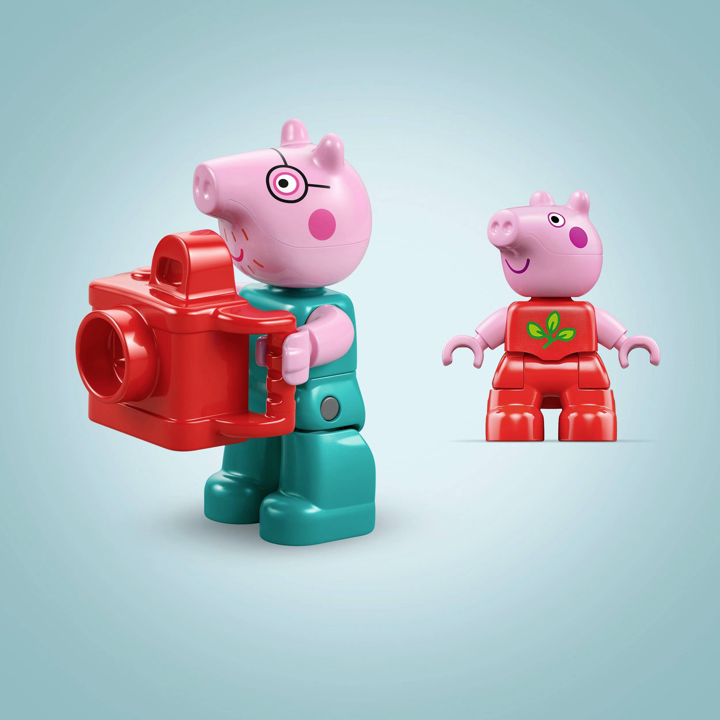 Zwei Spielfiguren, die wie Schweine aussehen: Eine trägt grüne Kleidung und hält eine rote Kamera, die andere hat rote Kleidung.