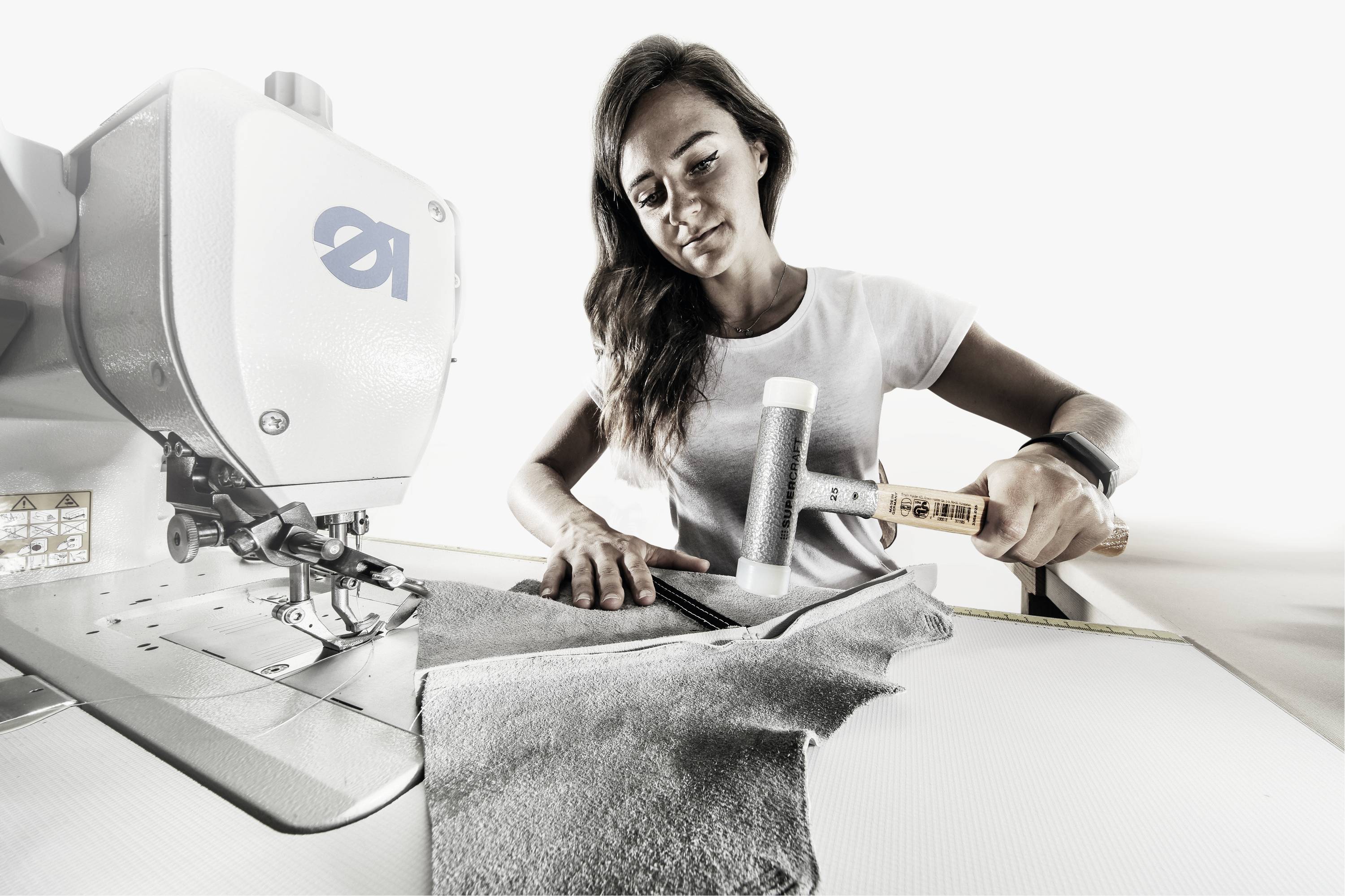 Eine Frau arbeitet an einer Nähmaschine, näht Stoffteile und konzentriert sich auf ihre Handarbeit in einer hellen Umgebung.