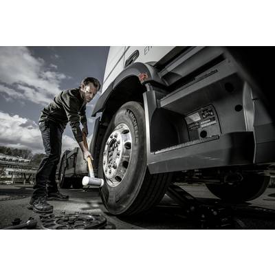 Ein Mechaniker überprüft mit einem Gummihammer die Reifen eines großen Lastwagens auf einem Parkplatz, um ihre Stabilität sicherzustellen.