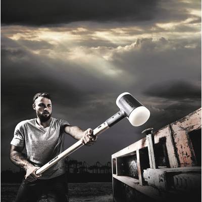 Mann in T-Shirt schlägt mit großem Hammer auf Container im industriellen Hafen, dramatischer Himmel im Hintergrund.