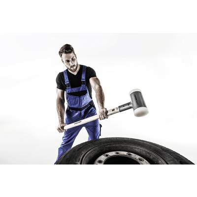 Ein Mann in blauer Arbeitskleidung benutzt einen großen Hammer, um auf einen Autoreifen zu schlagen.