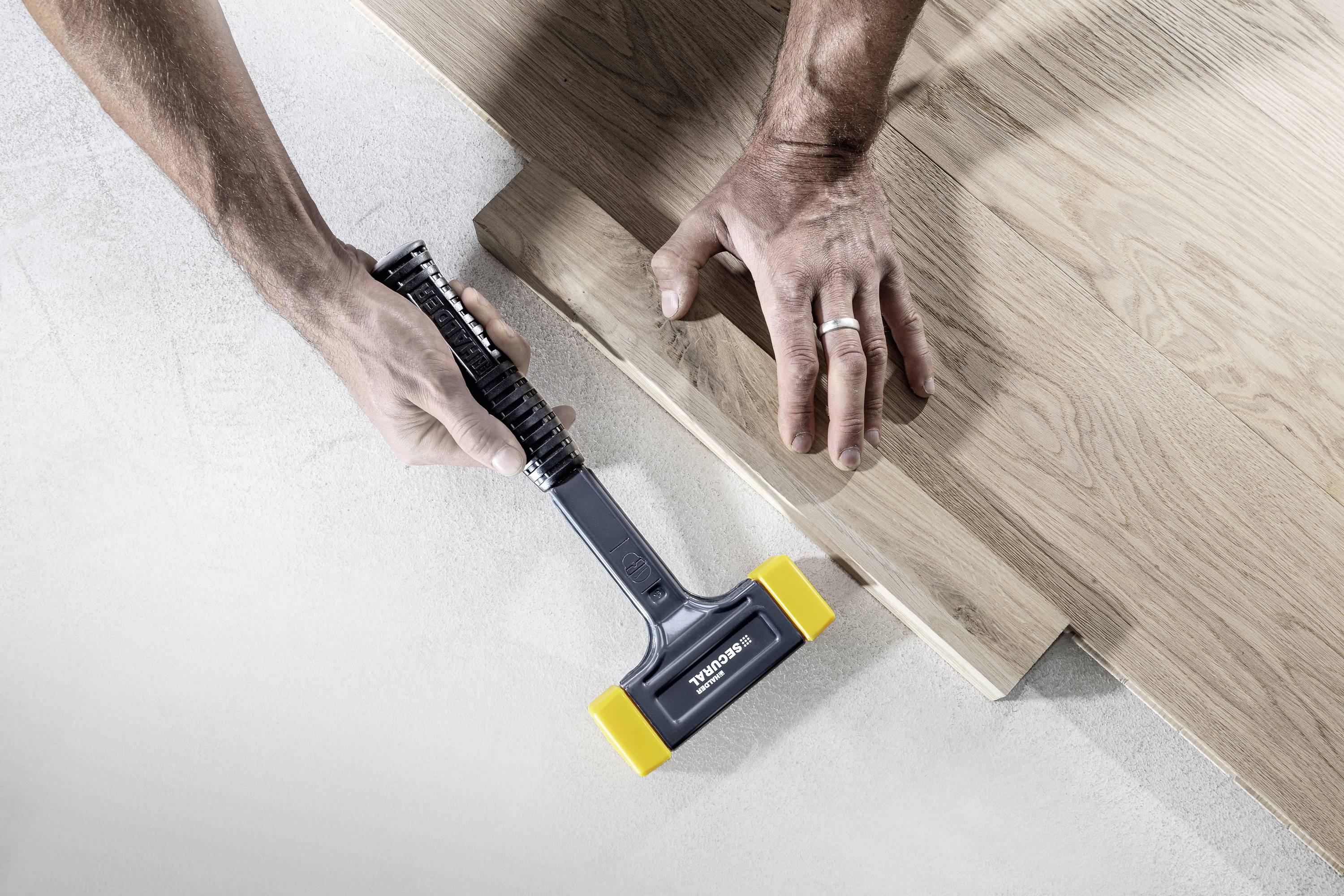 Eine Person justiert ein Stück Holzfußboden mit einem Hammer-Werkzeug.